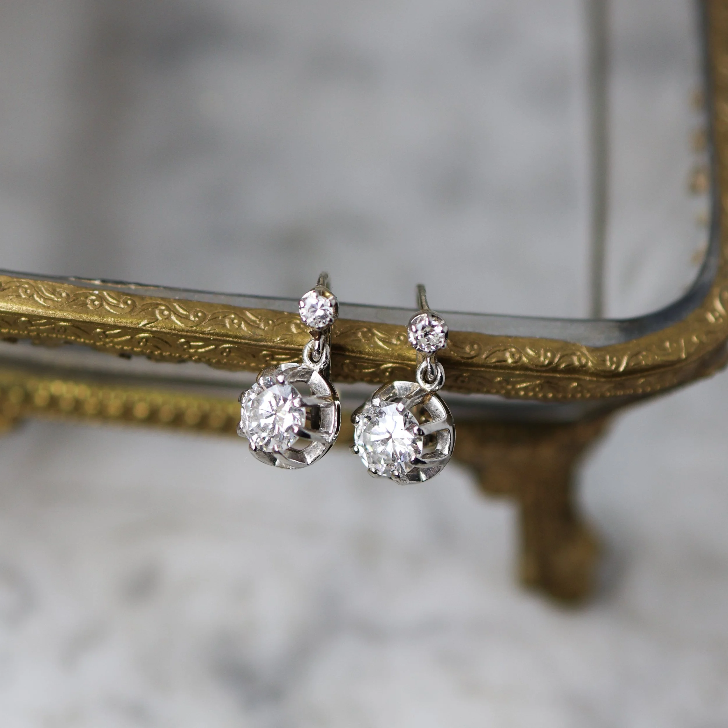 Boucles d'oreilles en platine avec des diamants posées sur un présentoir ancien avec dorure