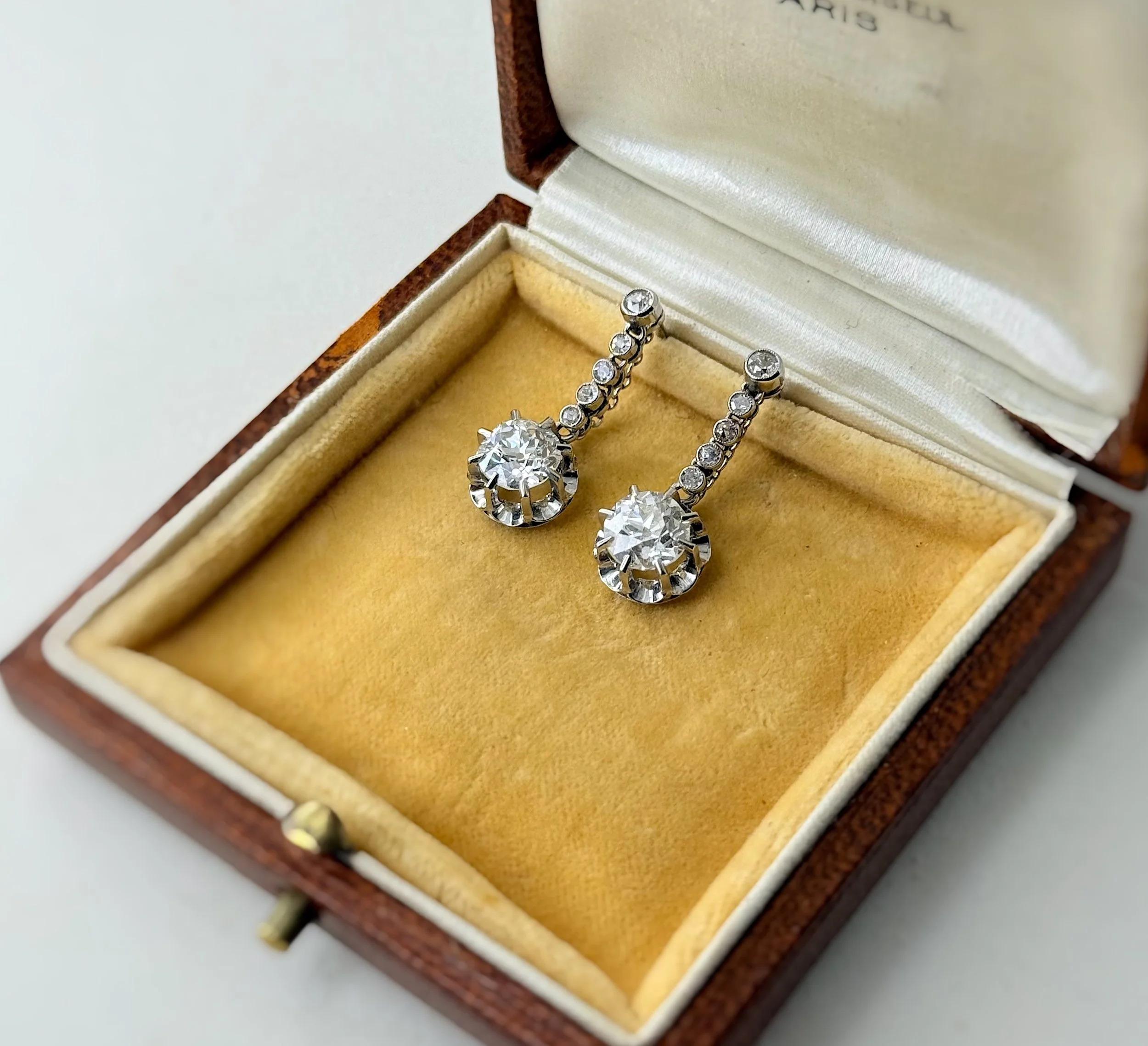 Boucles d’oreilles anciennes en argent serties de pierres blanches, présentées dans un écrin en bois à velours jaune