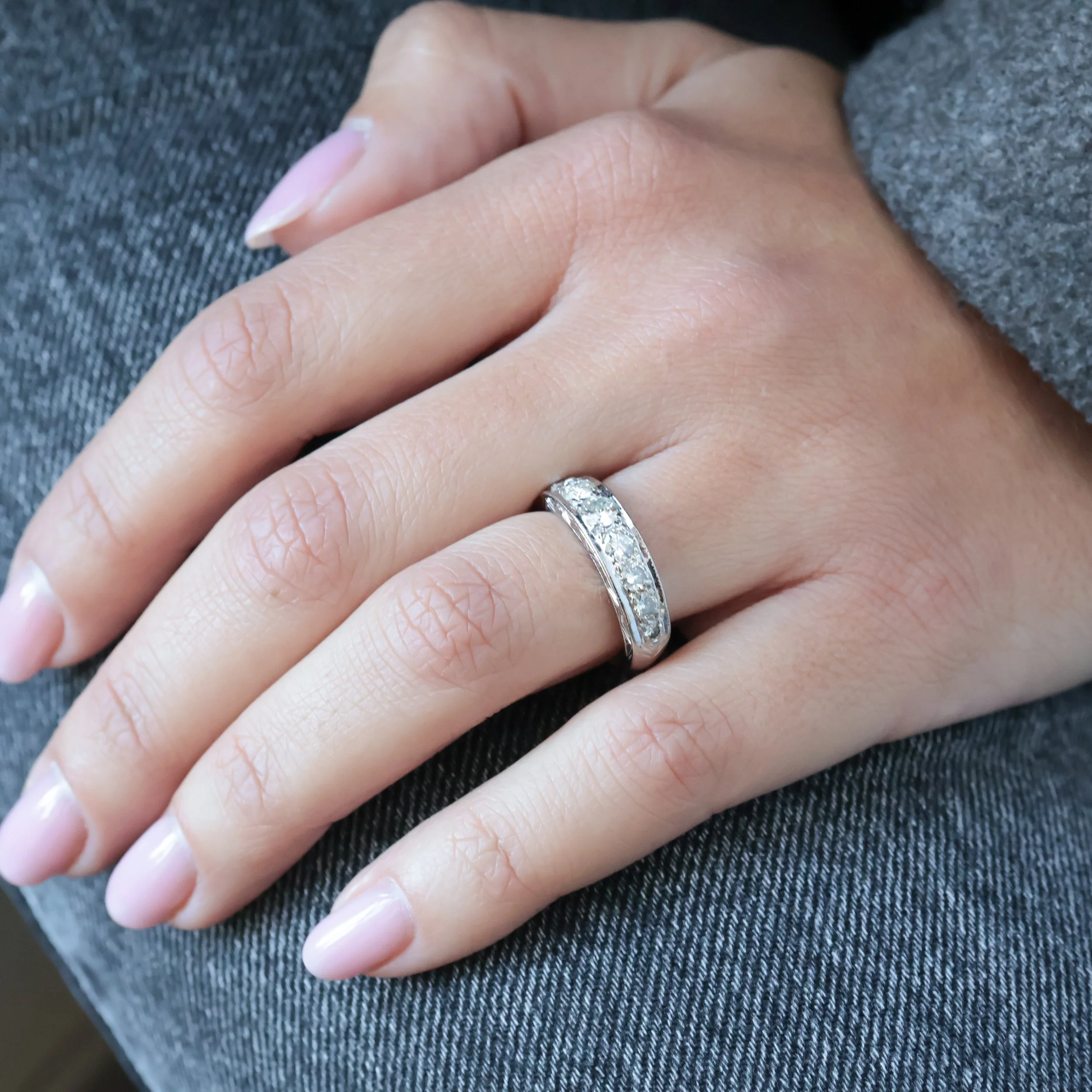 Main avec un alliance en argent ornée de diamants sur l'annulaire gauche, reposant sur un jean gris.