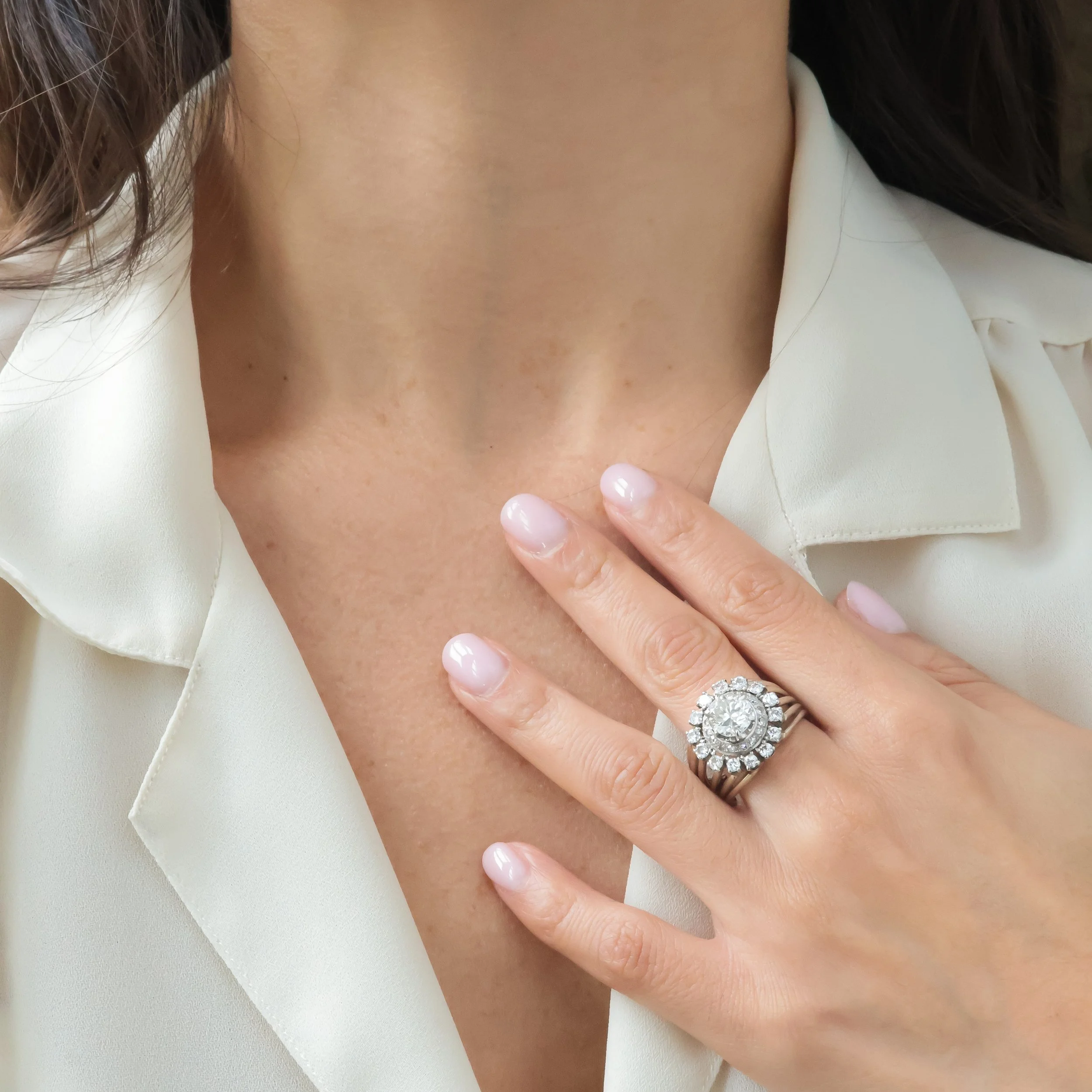 Une main portant une bague en diamant posée sur le décolleté d'une femme portant une chemise blanche.