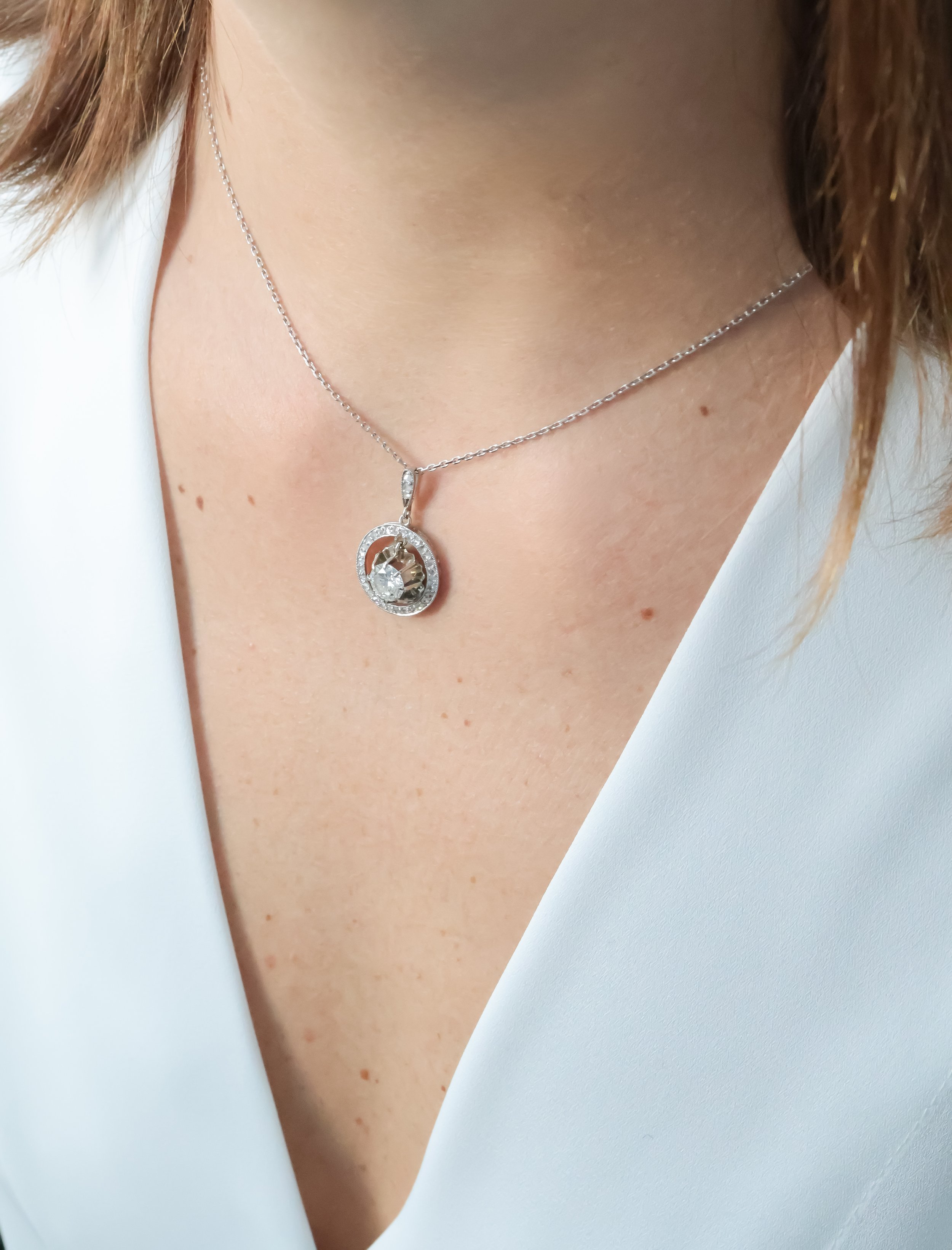 Collier en argent avec pendentif brillant porté par une femme, habillée d'une veste blanche.