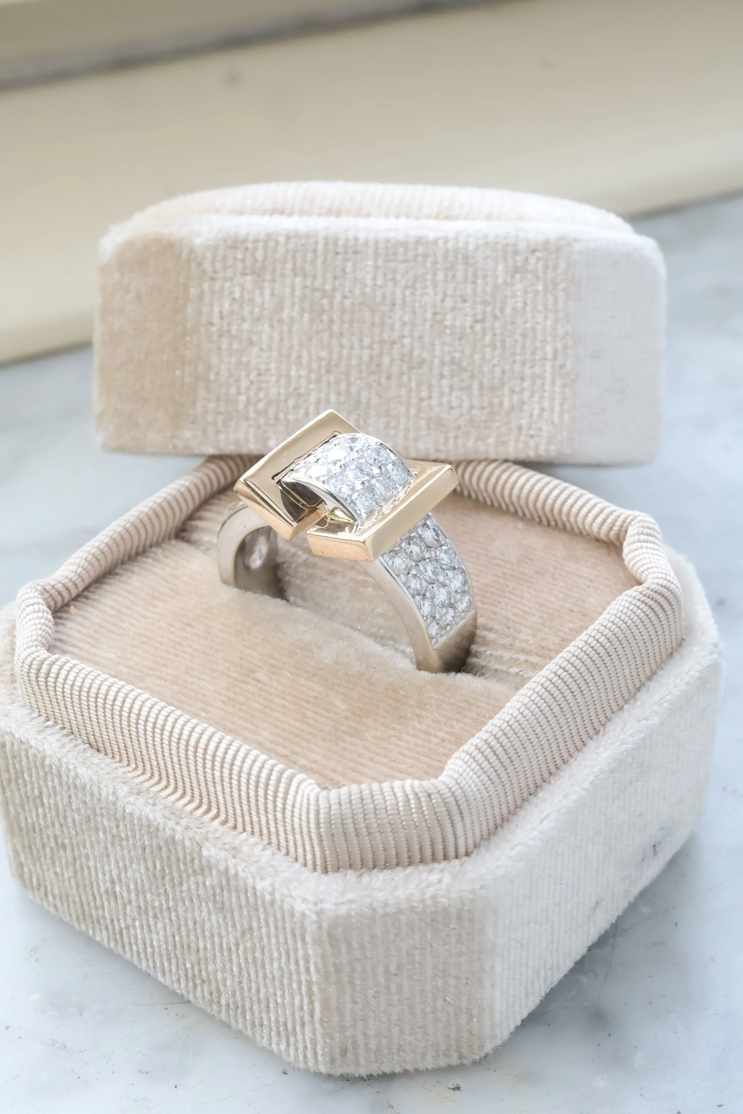 Bague en or et argent ornée de diamants, dans une boîte à bijoux en velours beige.