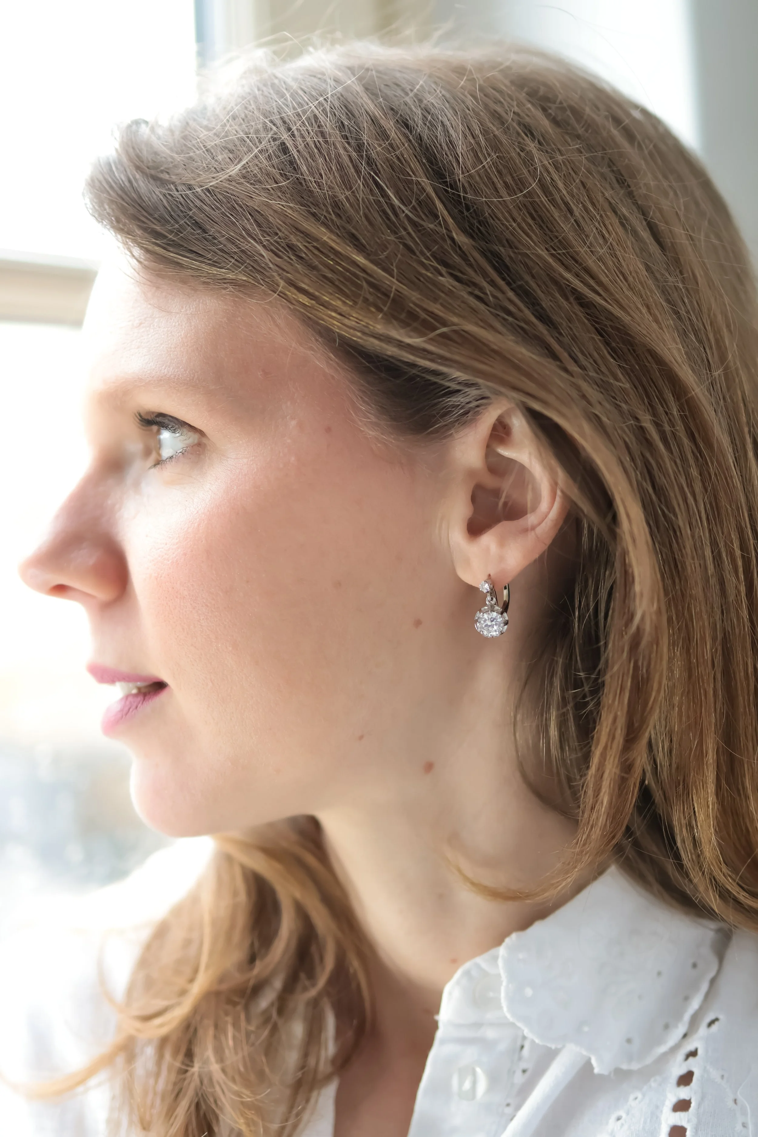 Portrait d'une femme avec boucle d'oreille en diamant, regardant vers la gauche, dans une pièce lumineuse.