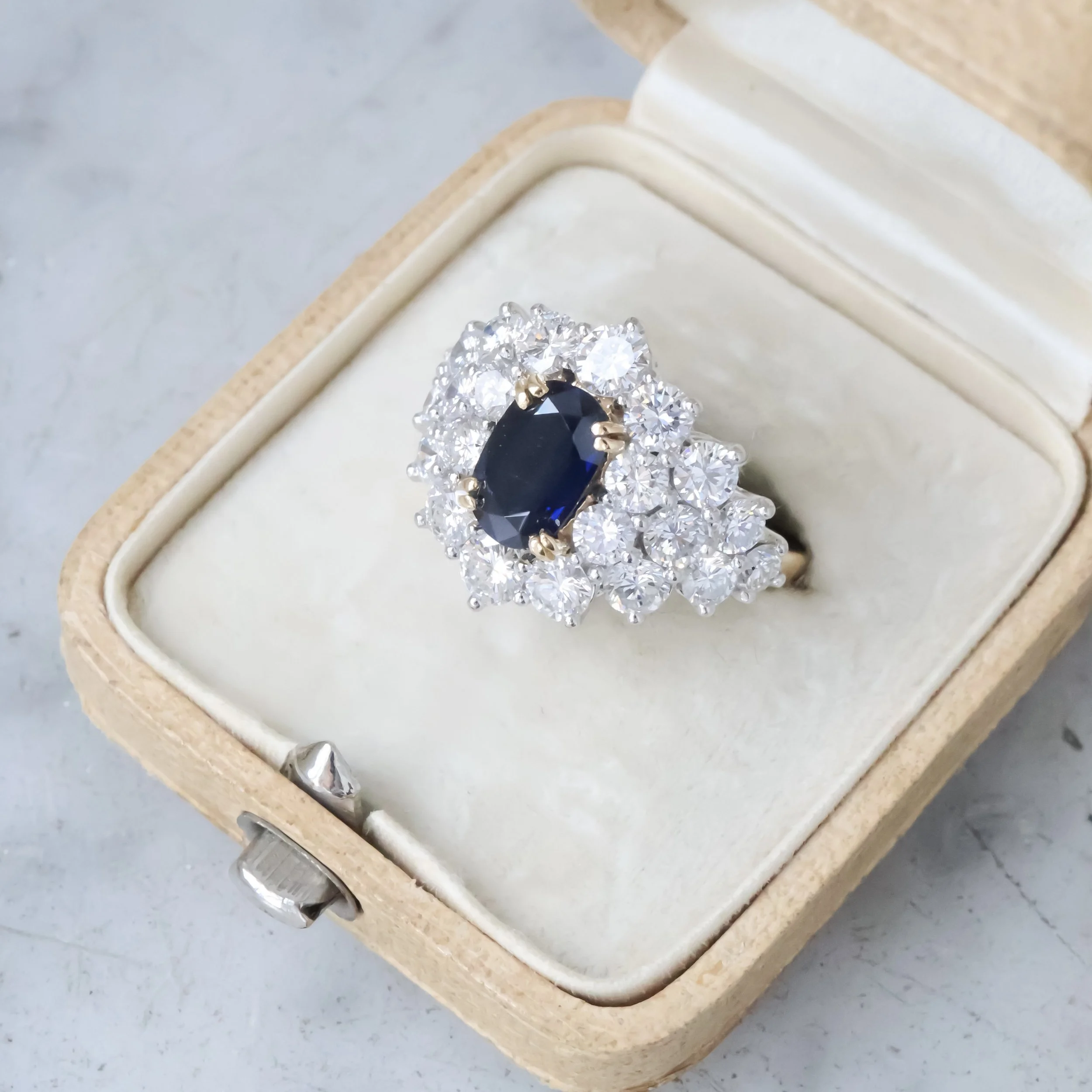 Bague avec une pierre centrale noire entourée de nombreuses diamants dans une boîte en bois.