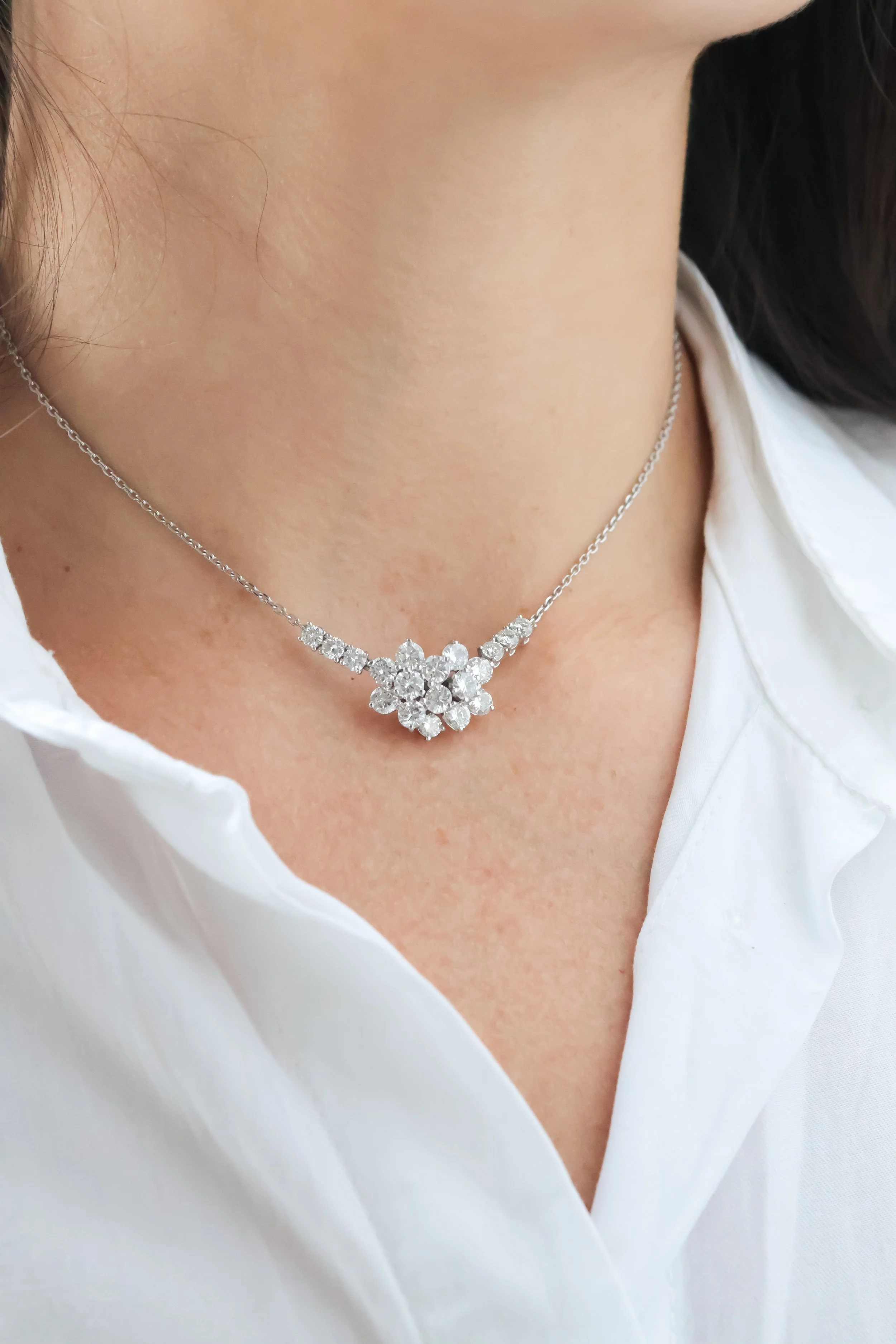 Collier en or blanc avec pendentif en forme de cluster de diamants porté par une femme en chemise blanche.