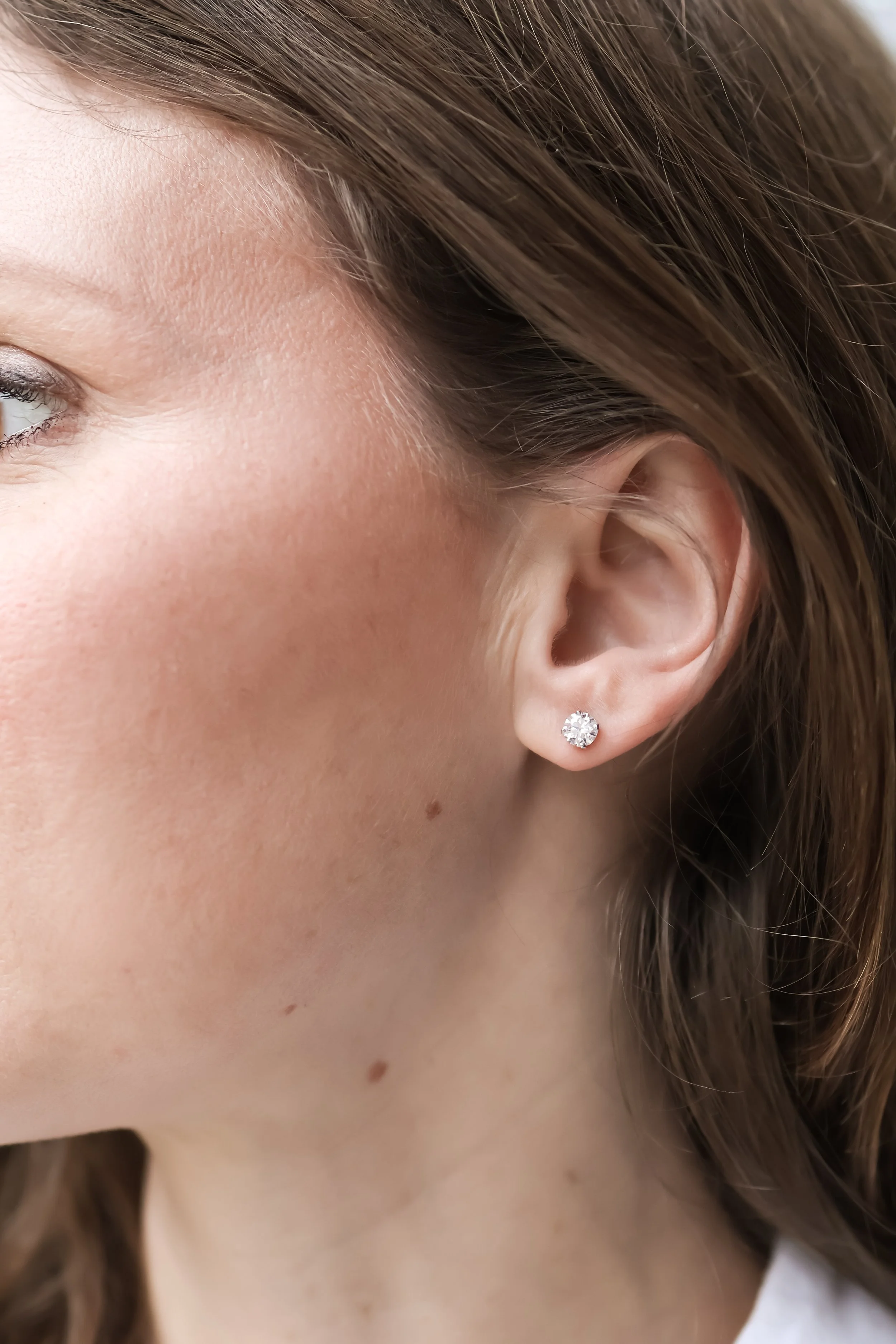 Focus sur une oreille féminine portant une boucles d'oreilles en diamant, avec une peau claire et des cheveux châtains.