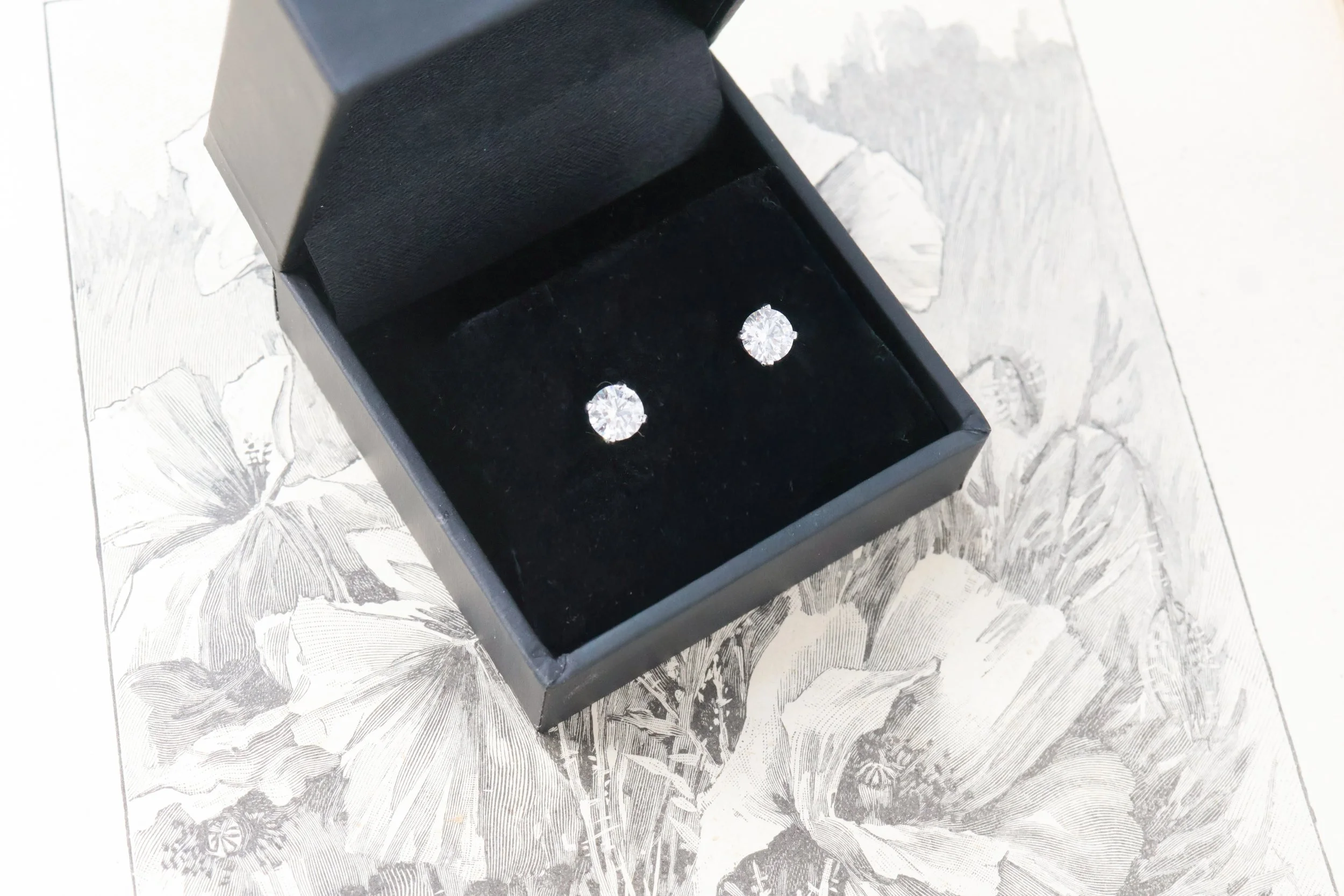 Une paire de boucles d'oreilles en diamants dans une boîte noire posée sur un livre ancien 