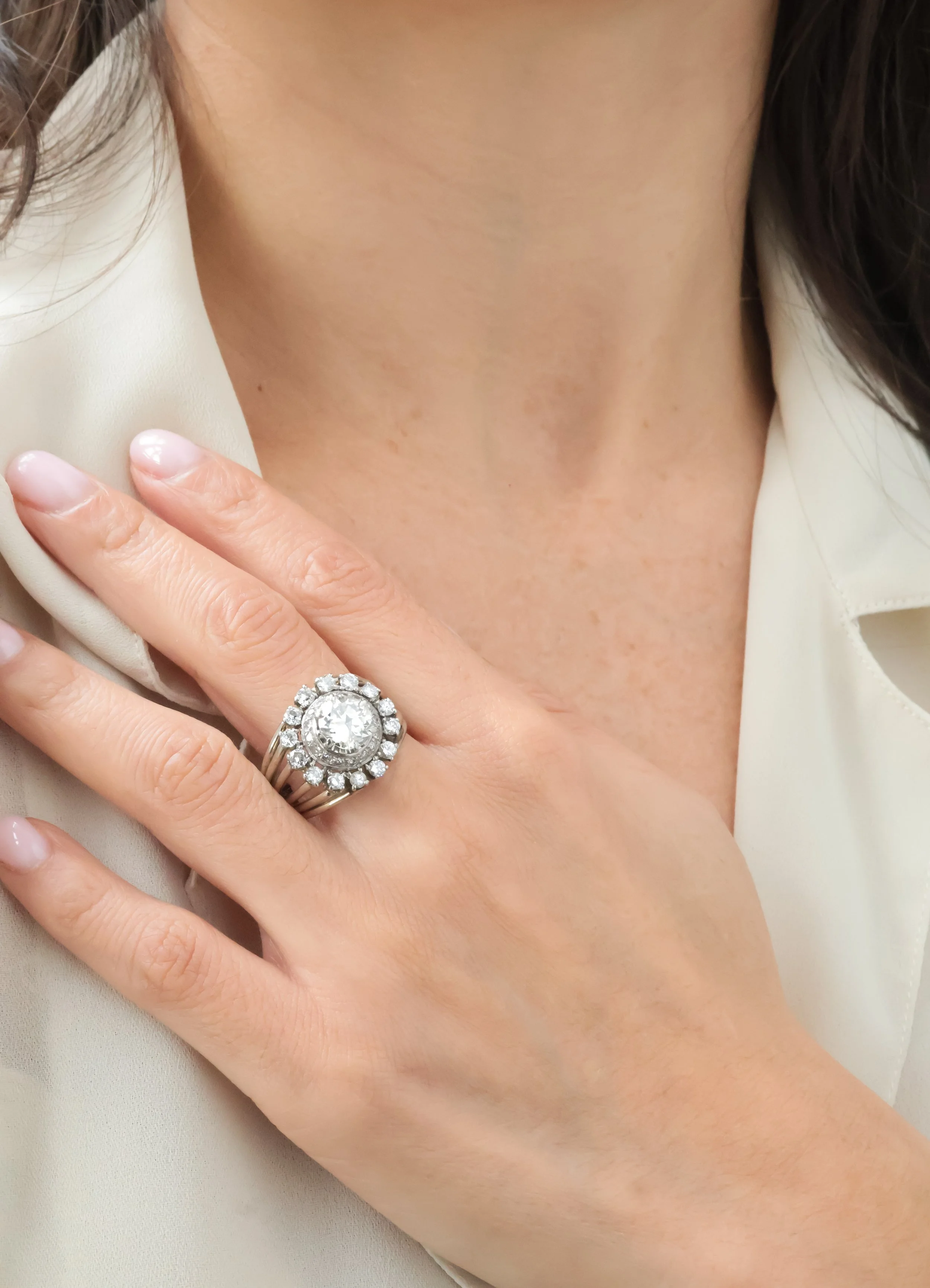 Main d'une femme portant une bague entourée de diamants, posé sur la poitrine, avec une chemise blanche ouverte