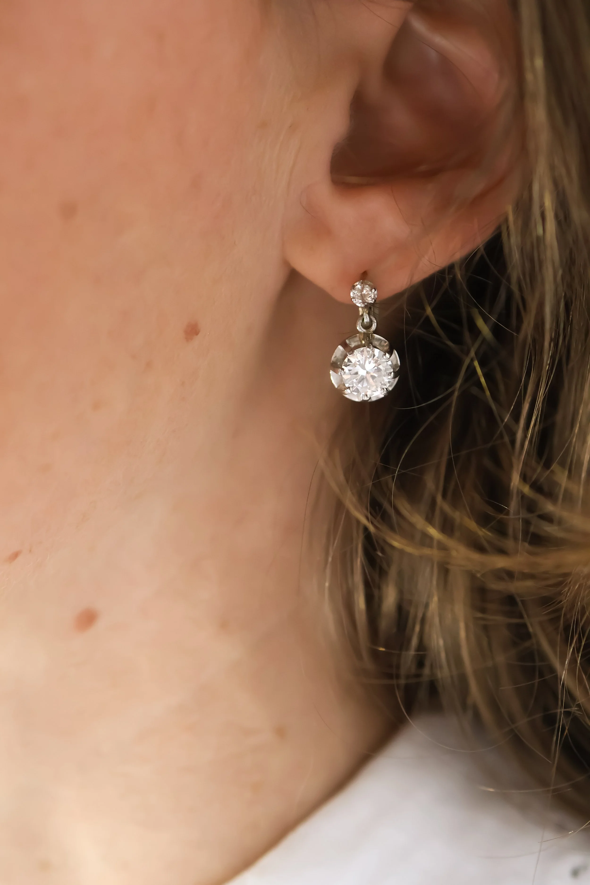 Boucle d'oreille avec deux diamants, porté par une personne avec des cheveux châtains et une peau claire, vu en gros plan sur l'oreille et le cou.