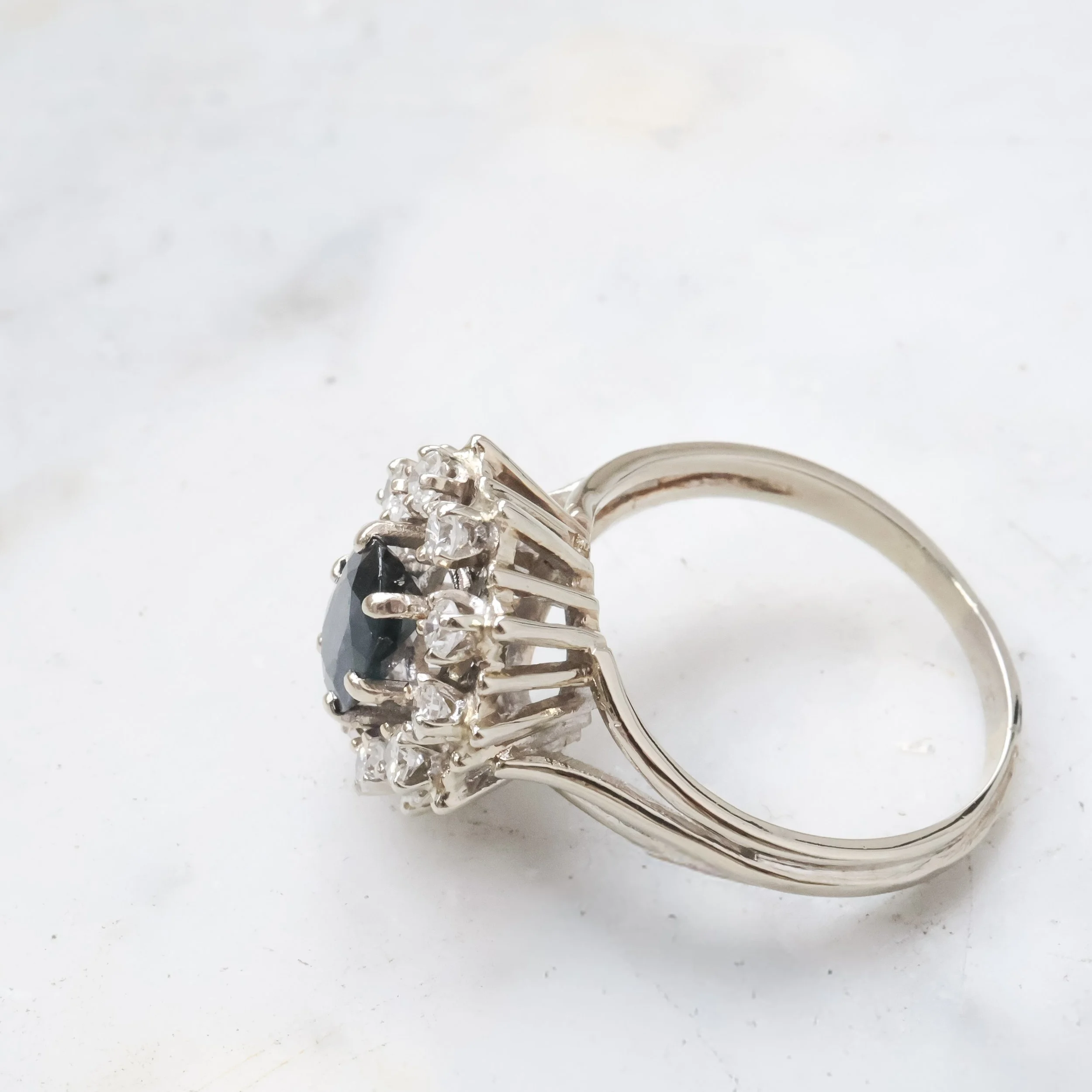 Bague en or blanc avec une pierre noire centrale entourée de diamants.