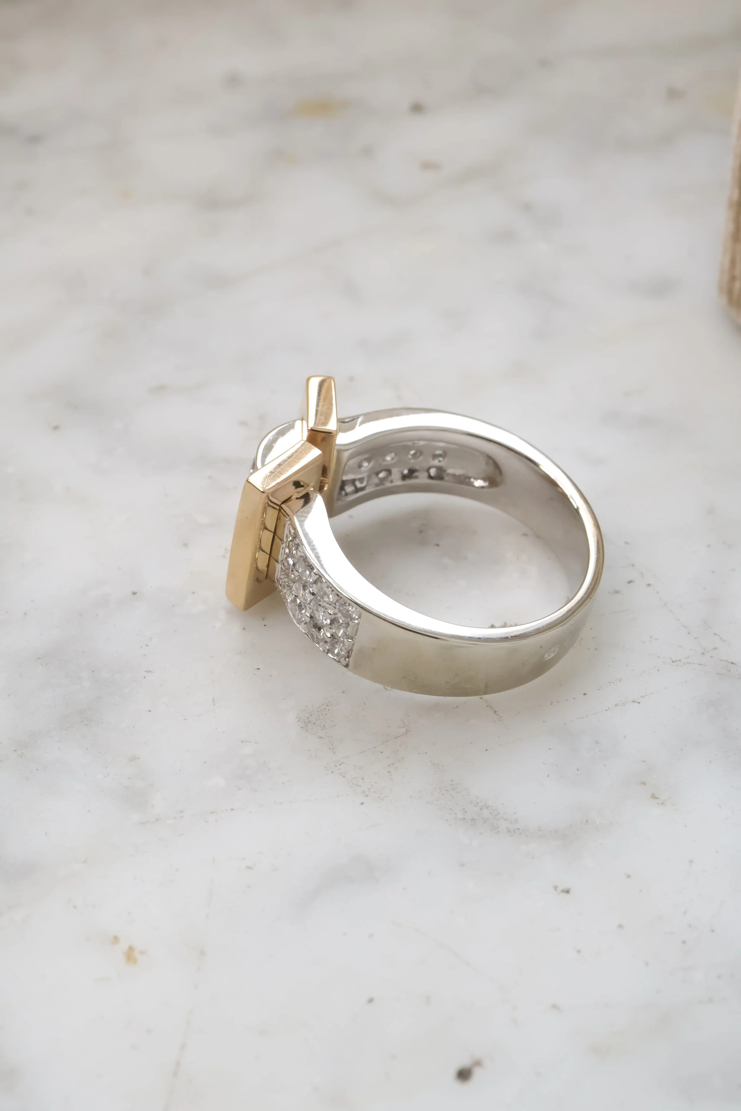 Bague en argent avec des détails en or et ornée de petits diamants, posée sur une surface de marbre.