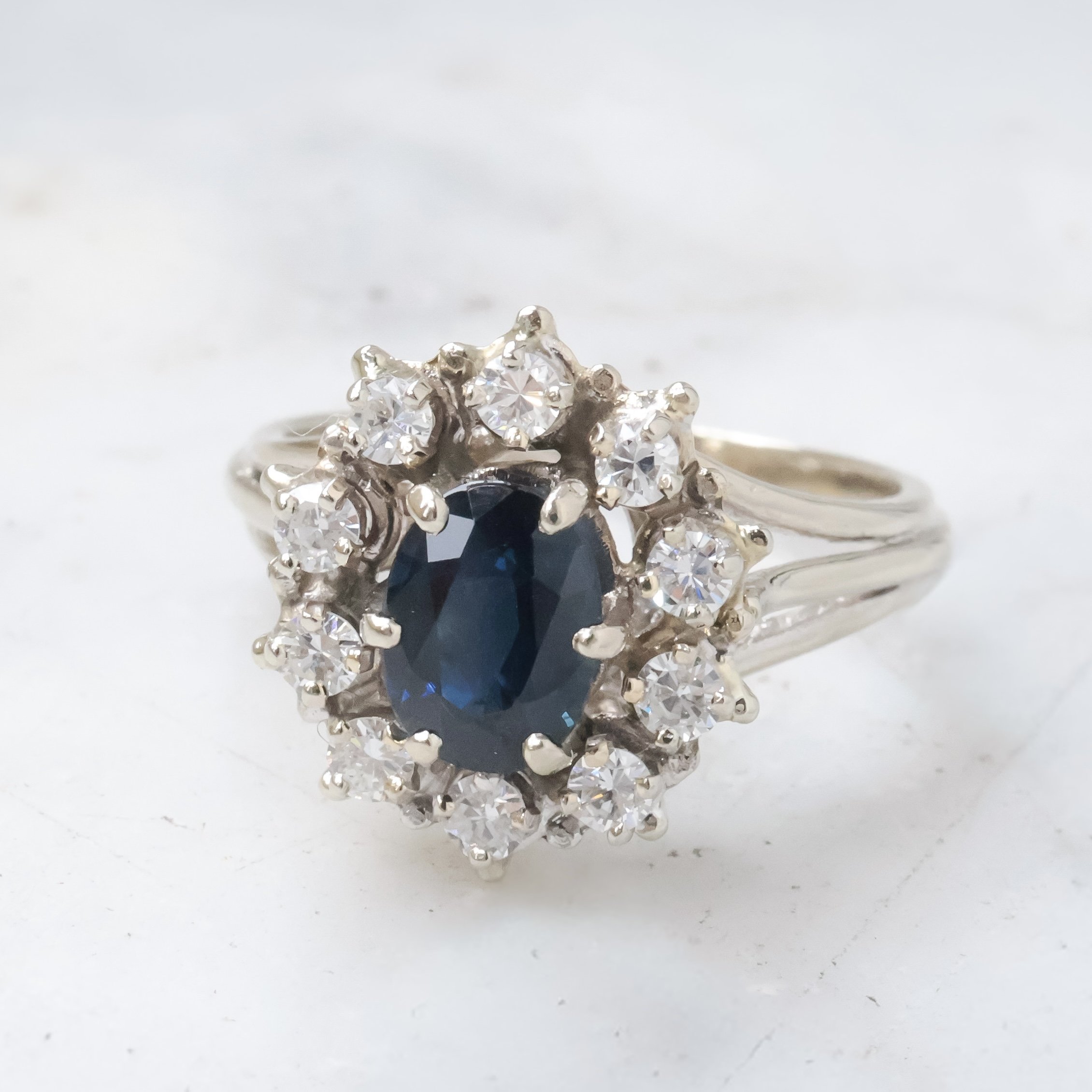 Bague en or blanc avec un saphir oval et entourée de diamants.