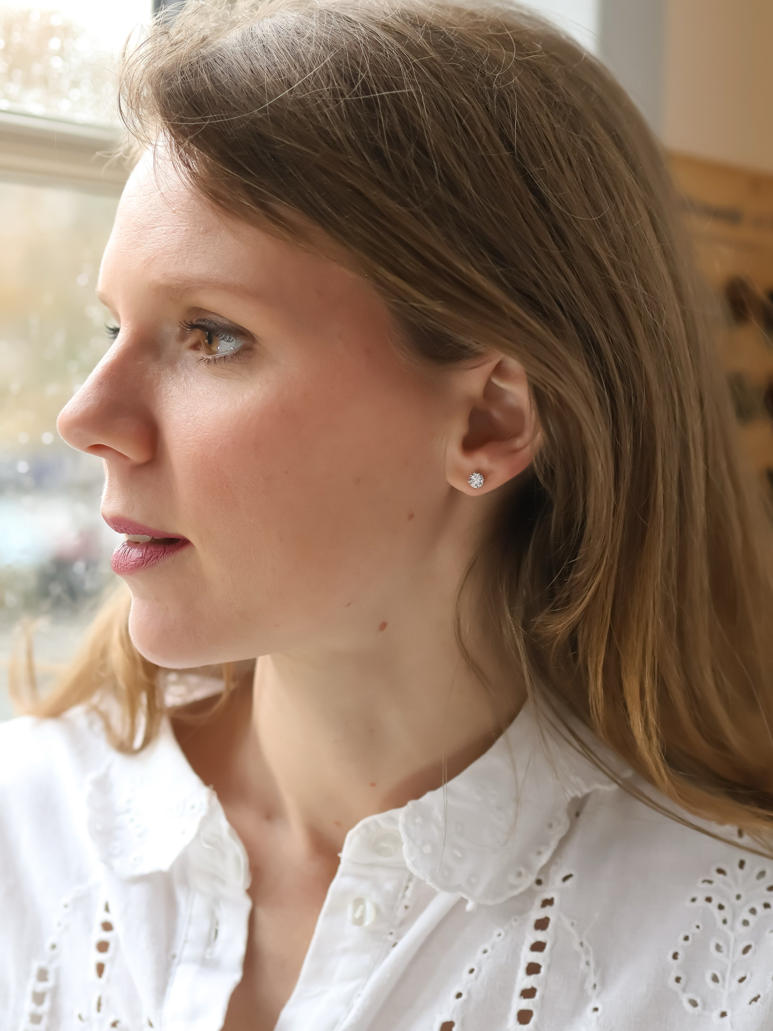 Une jeune femme aux cheveux blond posant devant une fenêtre, la jeune femme portant des boucles d'oreilles ornées de diamants