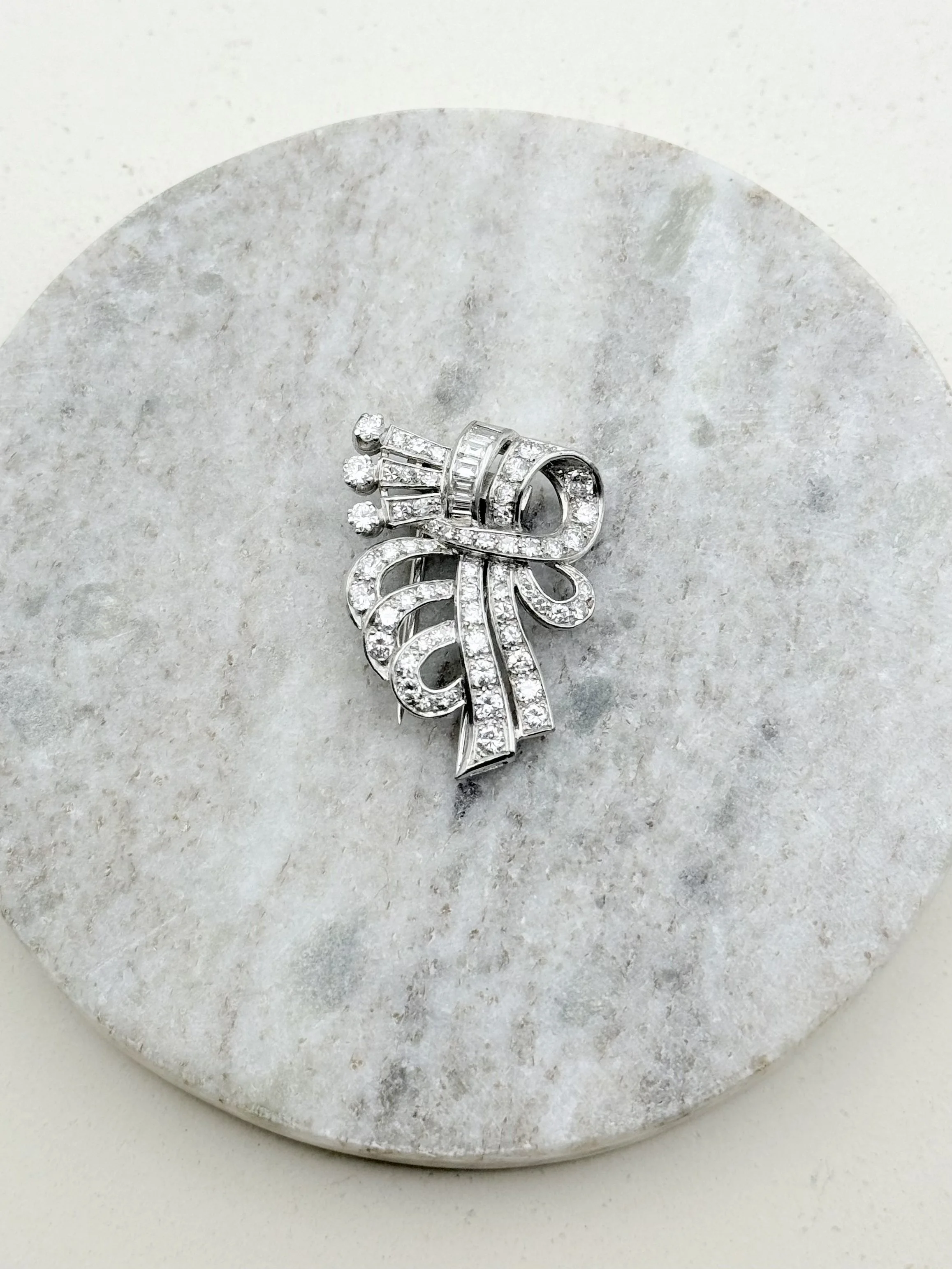 Broche ancienne en forme de nœud en or blanc sertie de diamants, posée sur fond minéral