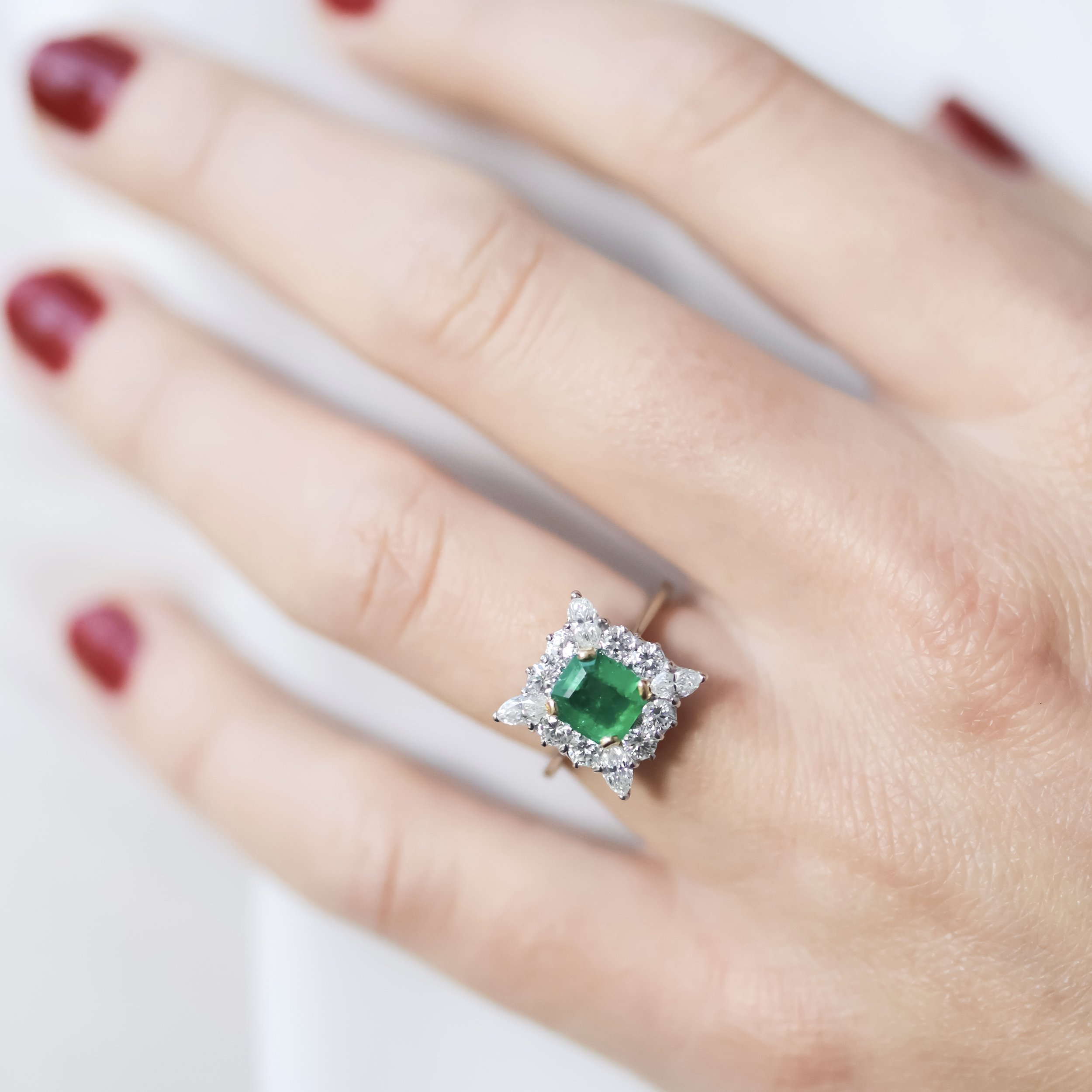 Bague ancienne en or blanc sertie d’une émeraude entourée de diamants, portée à la main
