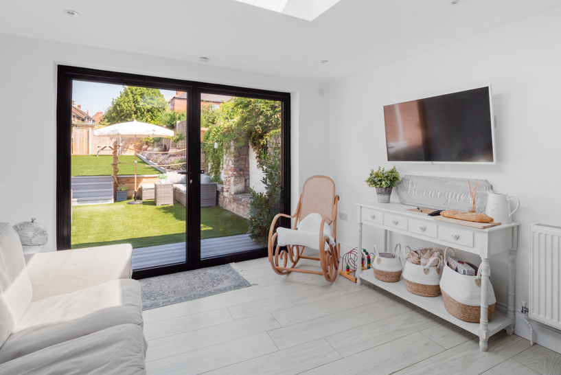 Living room with sliding glass door opening to a backyard with a lawn, outdoor furniture, umbrella, and trees.