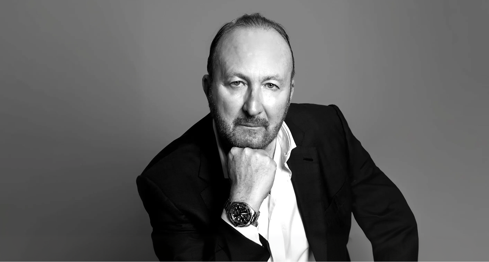 Ritratto in bianco e nero dell'Avvocato Luca Santa Maria. Descrizione: un uomo con barba, abbigliato con un completo nero e camicia bianca, che appoggia il mento sulla mano, con sfondo grigio uniforme.