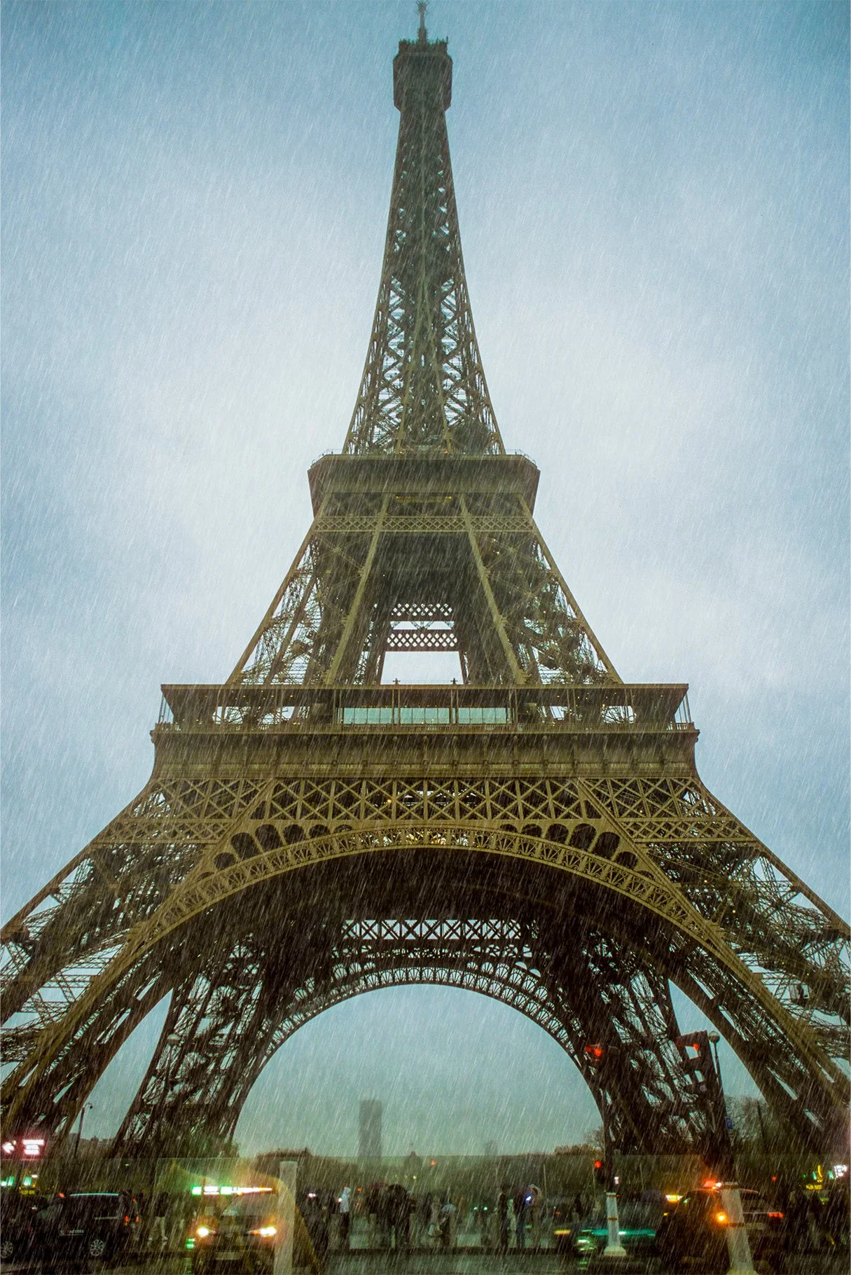 Eiffel Tower during a rainstorm with rain visibly falling and people walking nearby.