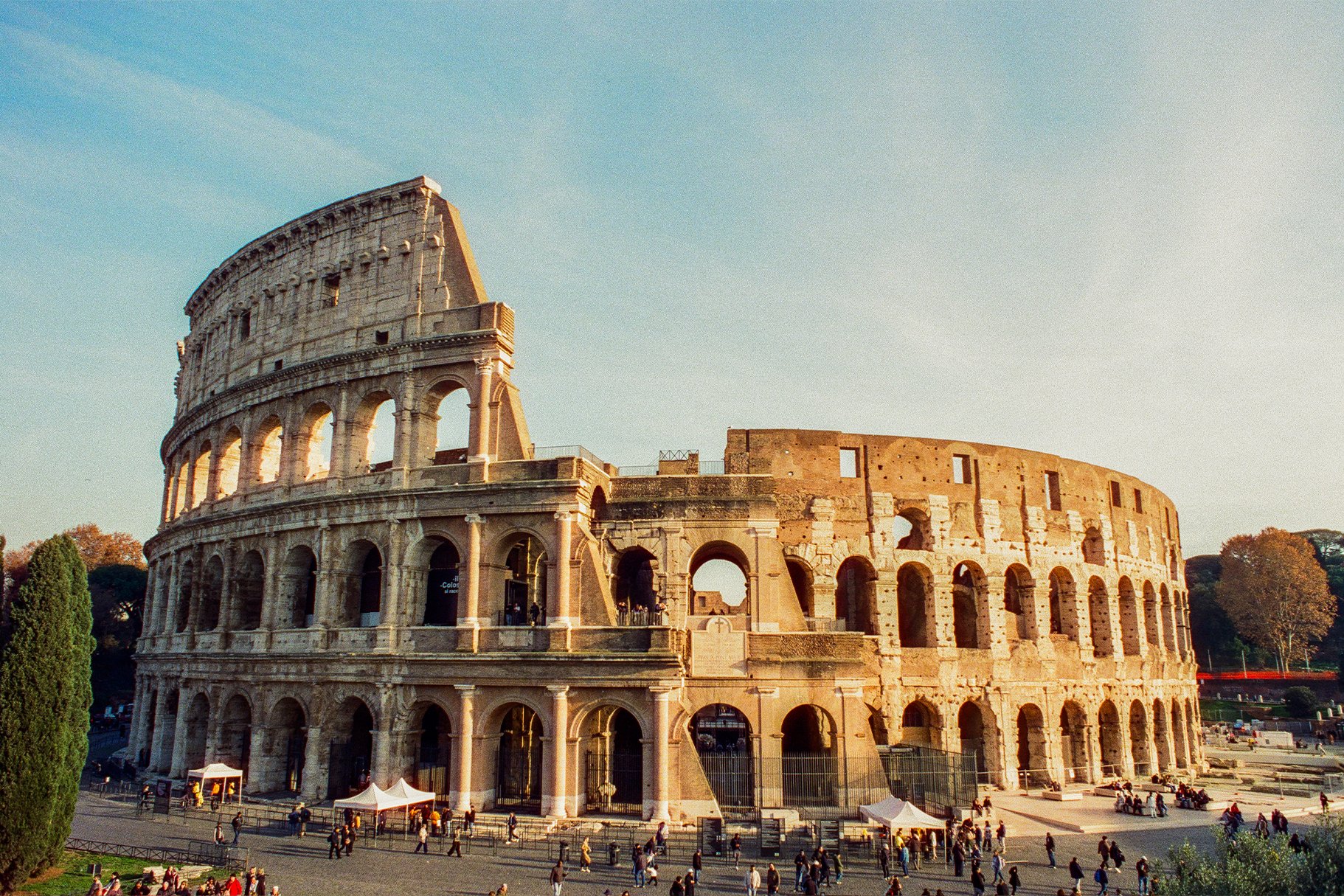 The Roman Colosseum in Rome, Italy, viewed in the late afternoon with people walking and sitting around the area.