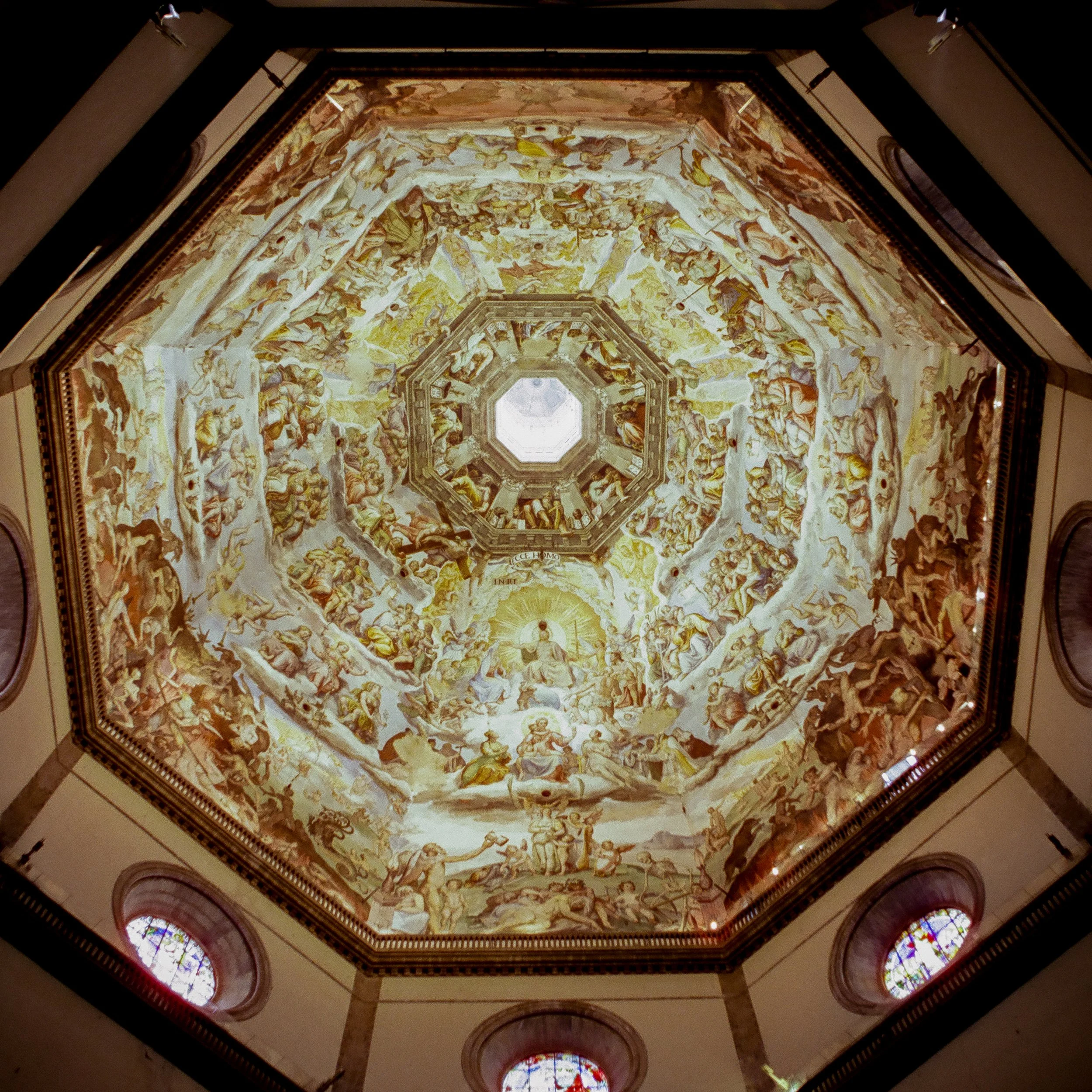 Ceiling of a church with elaborate frescoes and stained glass windows, viewed from below.