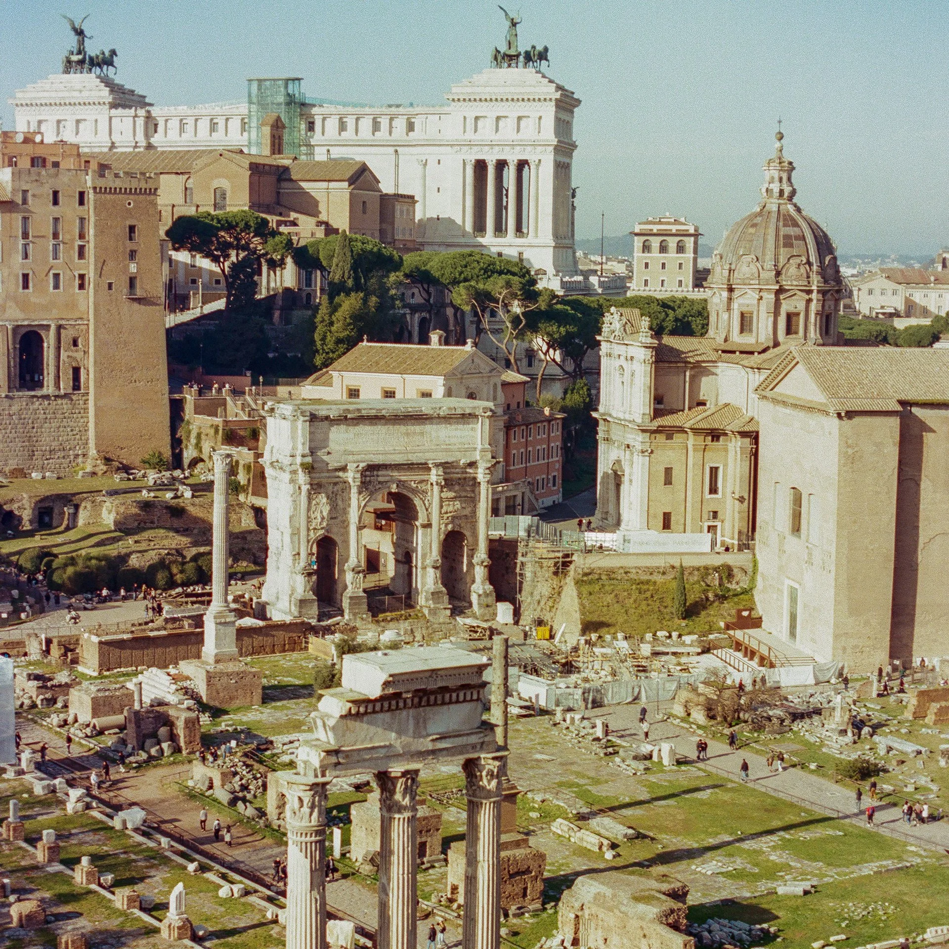 Ancient ruins and marble columns in a cityscape with historic buildings and greenery, likely in Rome, Italy.