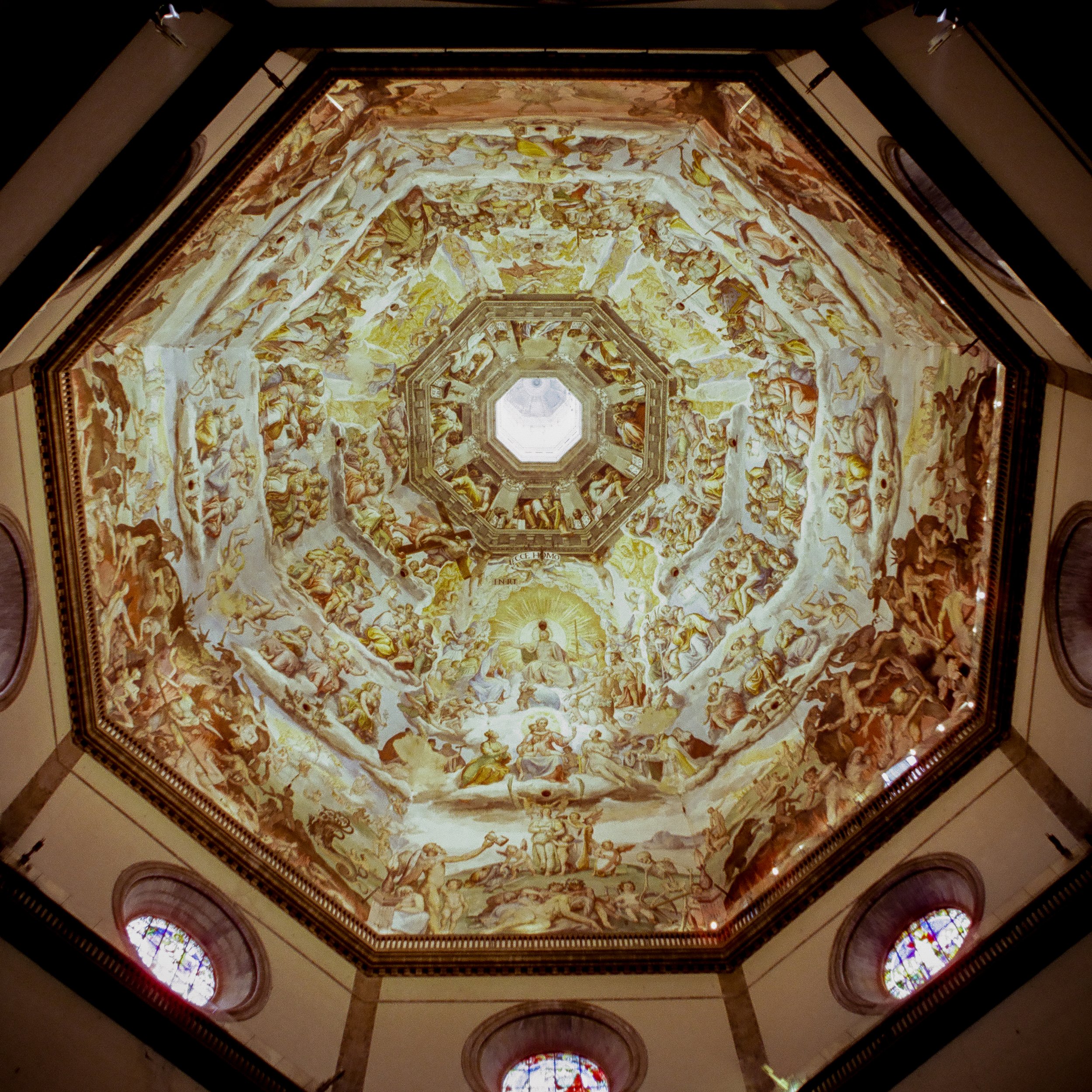 Ceiling of a church dome decorated with religious frescoes depicting angels, saints, and biblical scenes, with stained glass windows around the base.