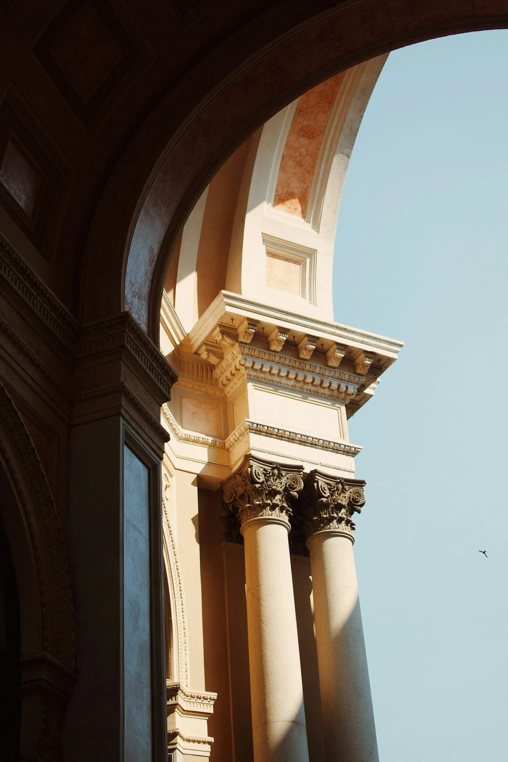 A view of classical architectural columns and arches with ornate details, set against a clear blue sky.