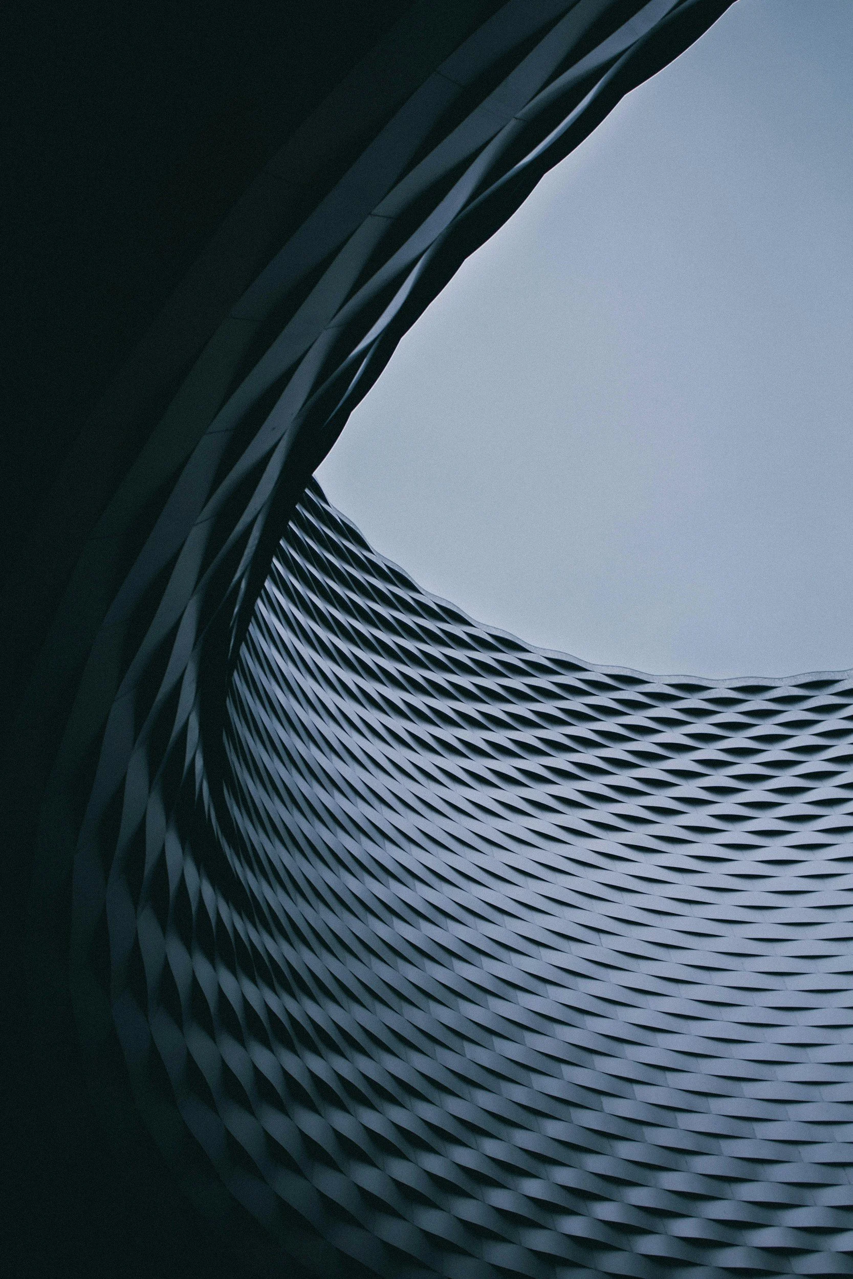 Looking up at a modern building with a wavy metallic exterior pattern and a bright sky in the background.