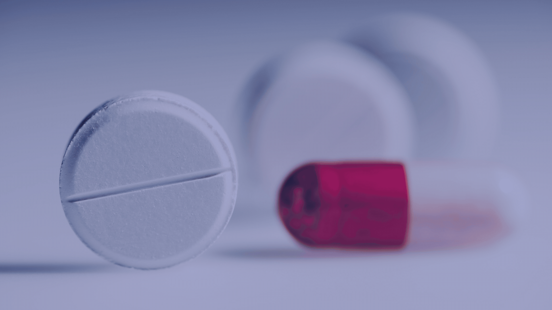 Close-up of a large white pill with a score line and a red capsule pill on a white surface.