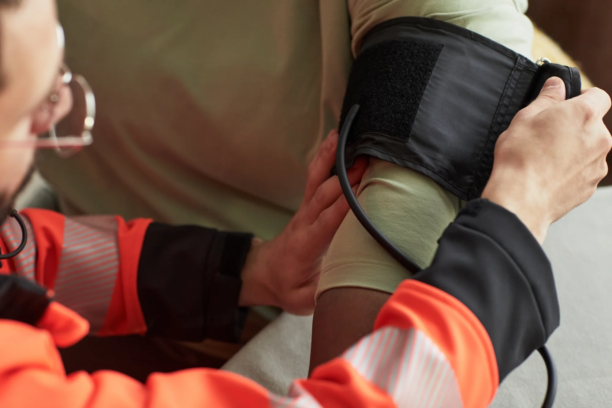 A healthcare worker in orange scrubs taking a person's blood pressure using a blood pressure cuff on their arm.