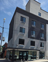 Modern multi-story building with a gray and black exterior, rectangular windows, and an overhang at street level