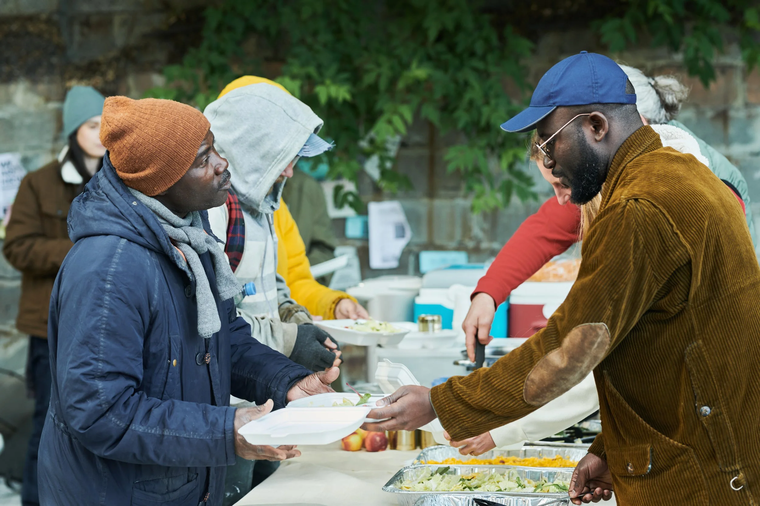 People at a food distribution event, handing food trays to each other, with a salad tray visible on the table.