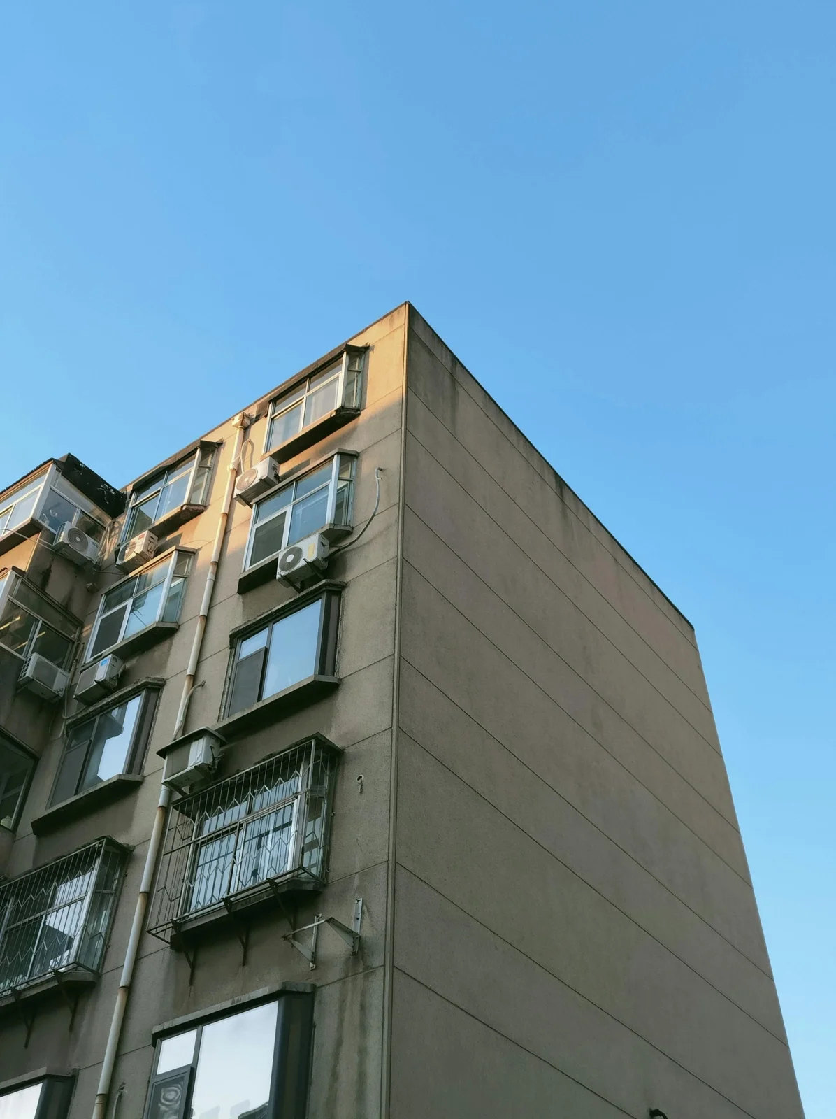 Apartment building with air conditioning units on windows, set against a clear blue sky.