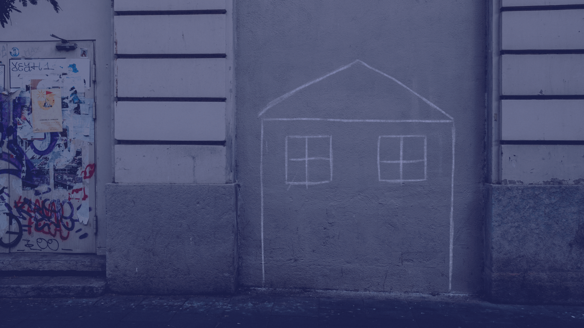 A concrete wall with graffiti art on a door and a chalk drawing of a house, with windows and a roof, on the wall.