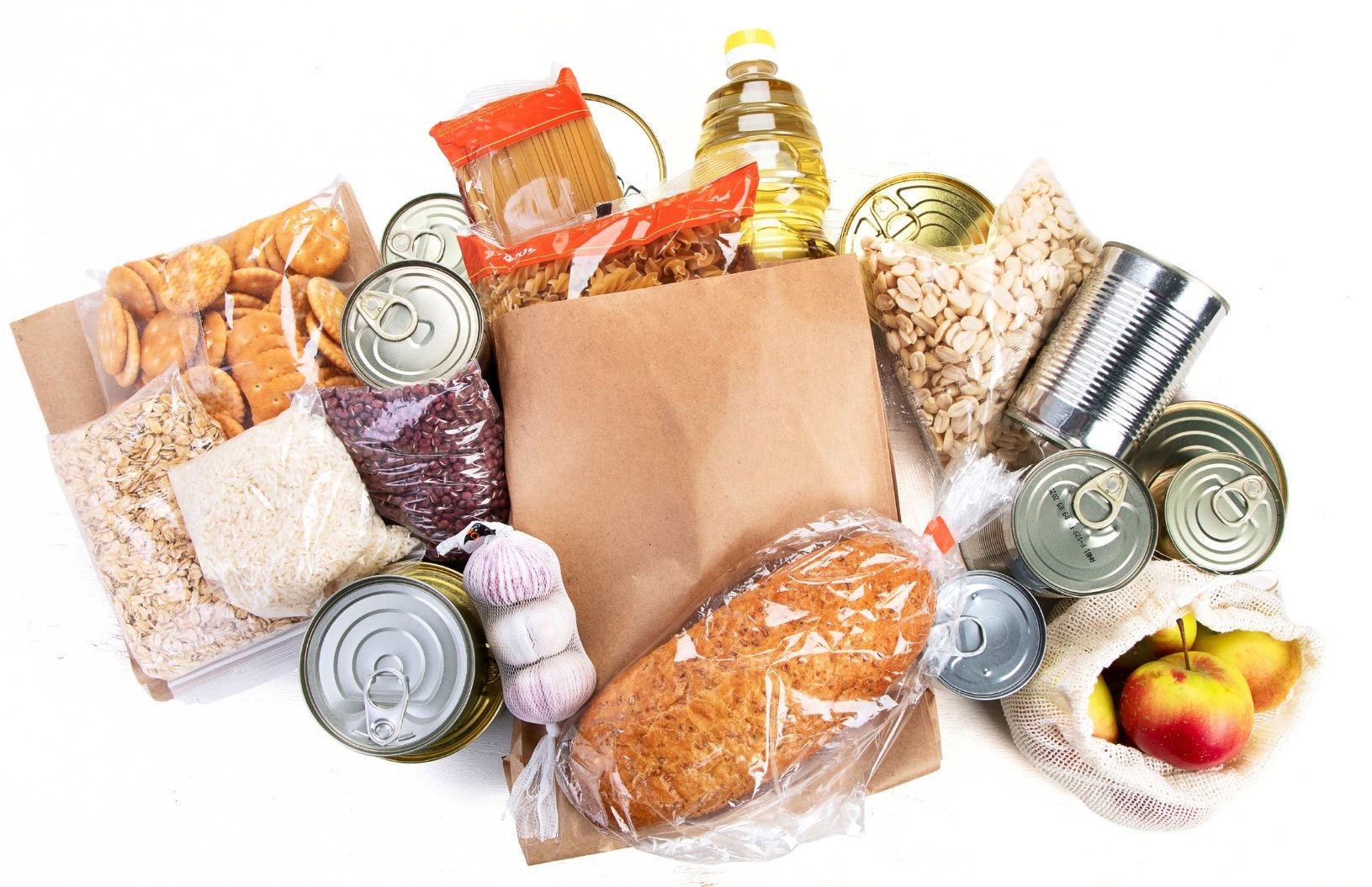 A collection of groceries including canned goods, pasta, rice, dried beans, snack foods, a loaf of bread, a bag of apples, and a paper bag, organized on a white background.