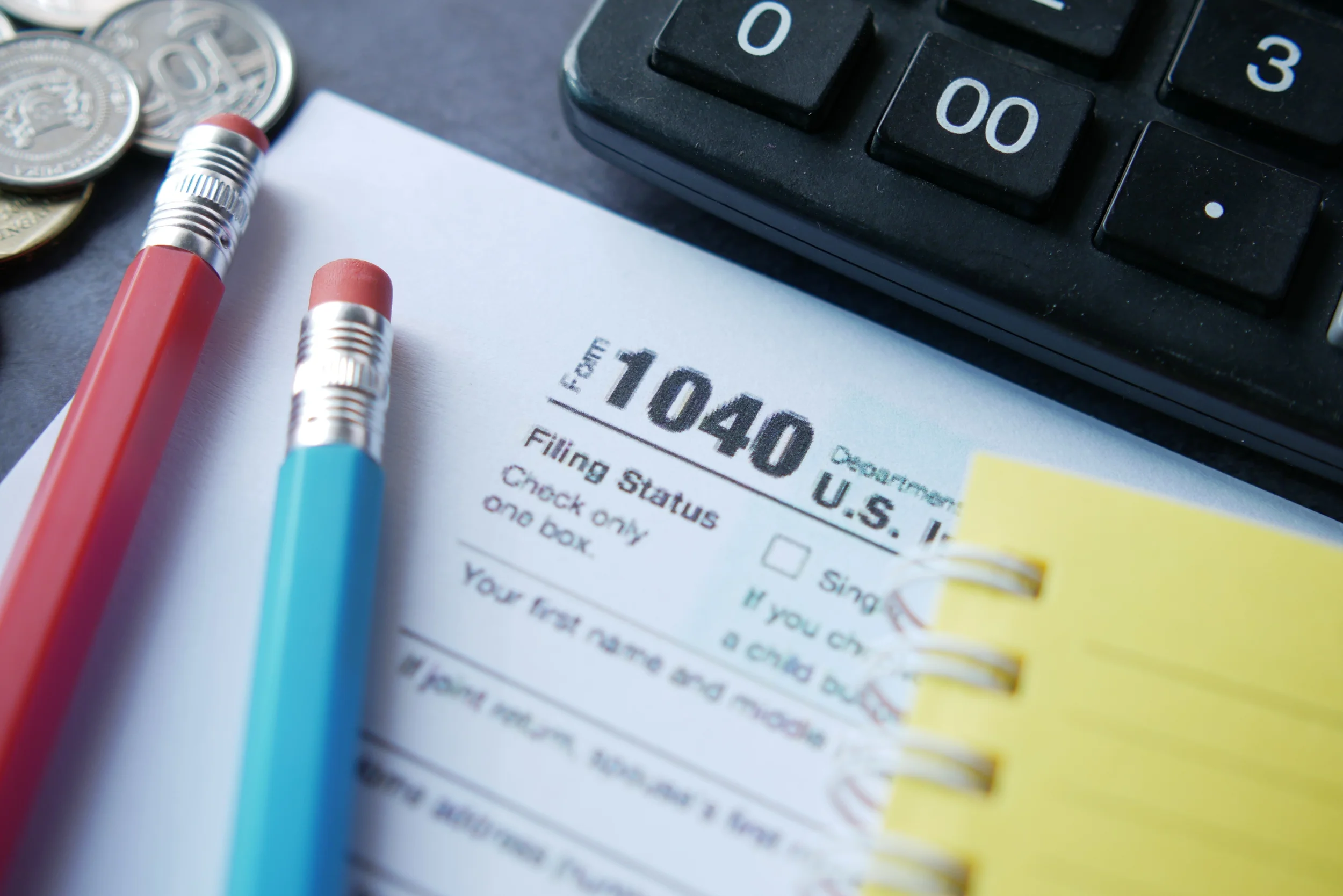 Close-up of a tax form, pens, coins, and a calculator on a desk, indicating financial or tax preparation work.