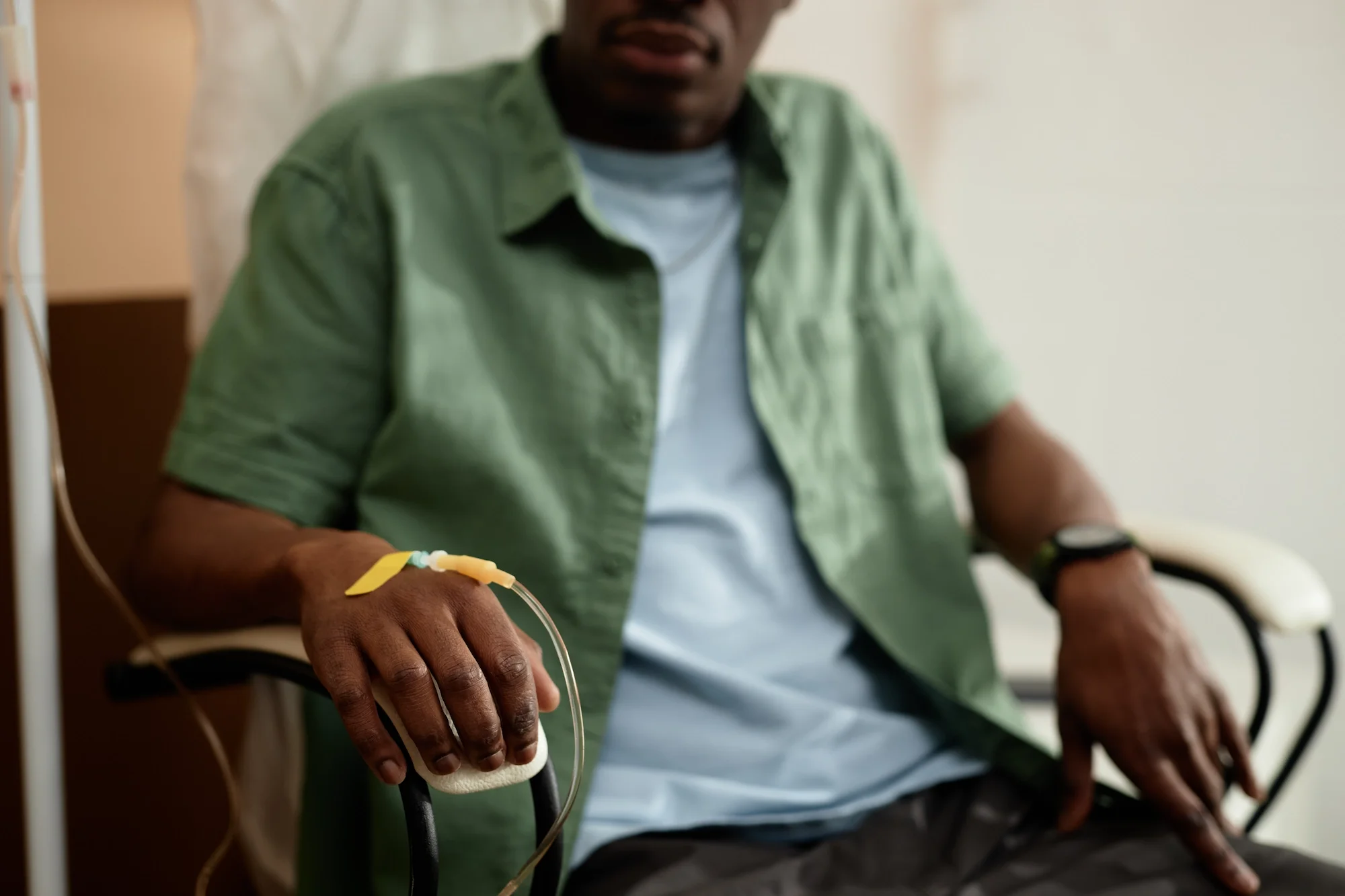 A person in a hospital bed receiving IV fluids, wearing a green shirt, with a medical bracelet and watch on the wrist.
