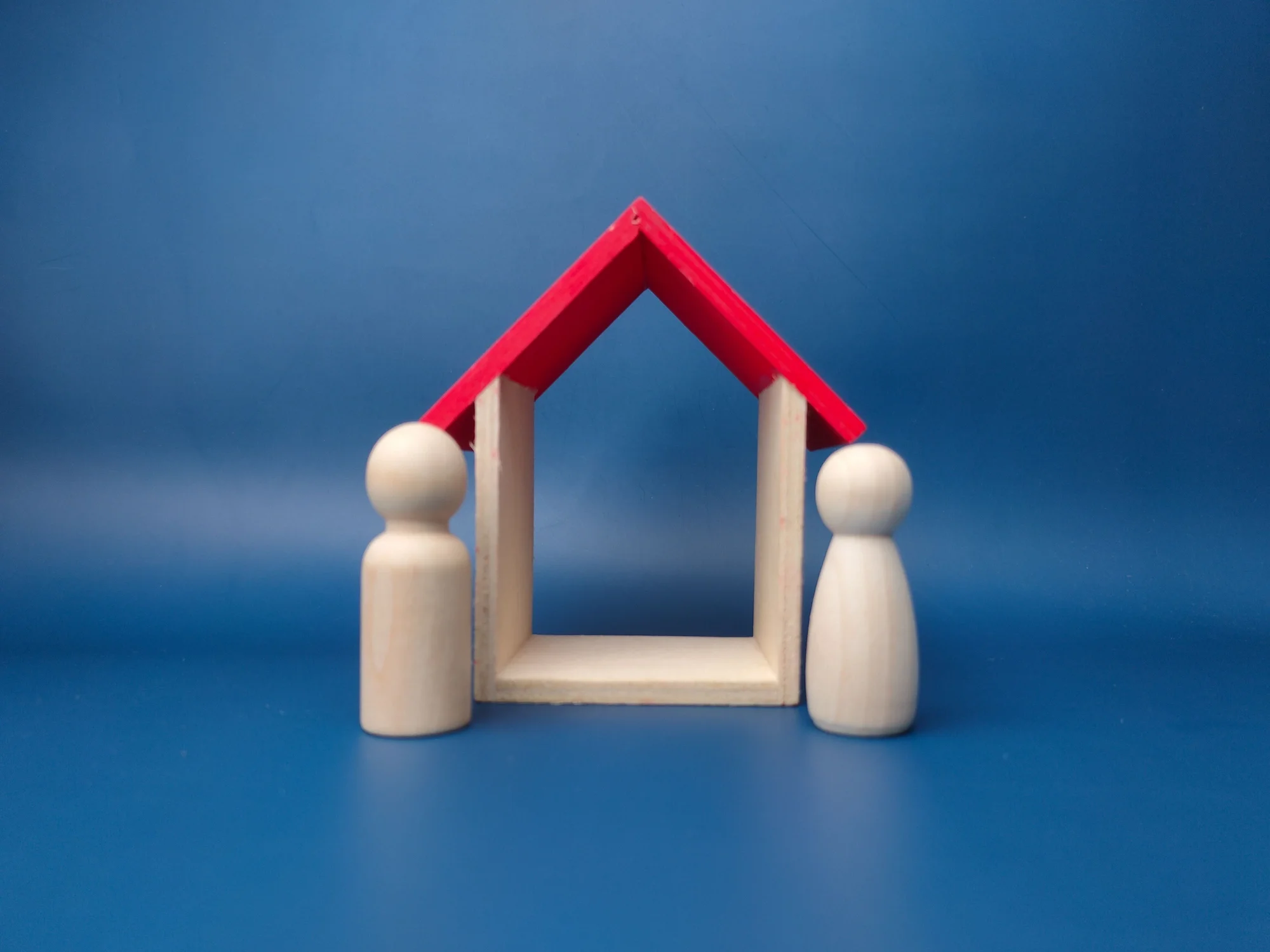 A small wooden house-like structure with a red roof and four white poles, against a blue background.