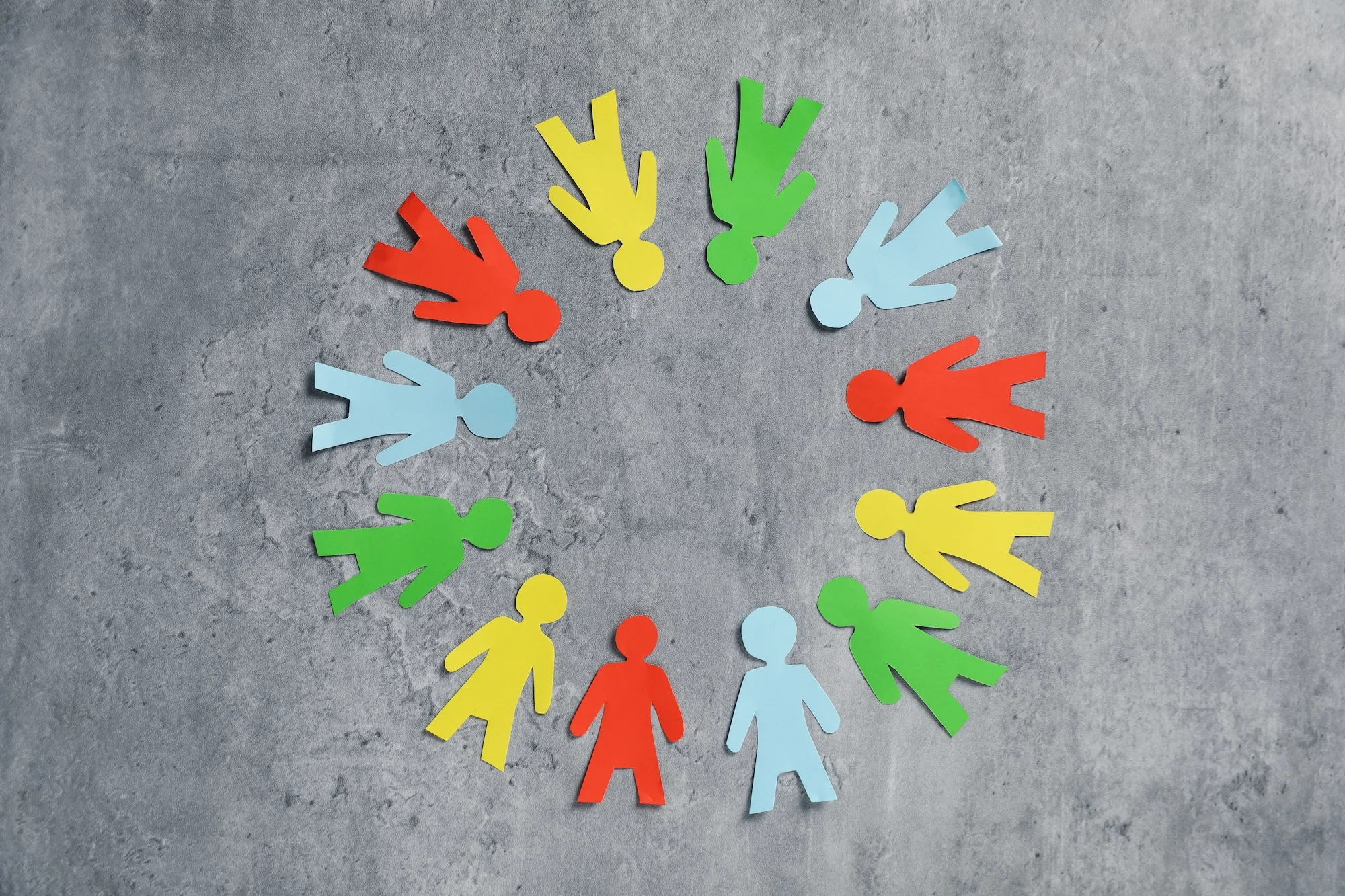 Colorful paper cutouts of human figures arranged in a circle on a gray surface.