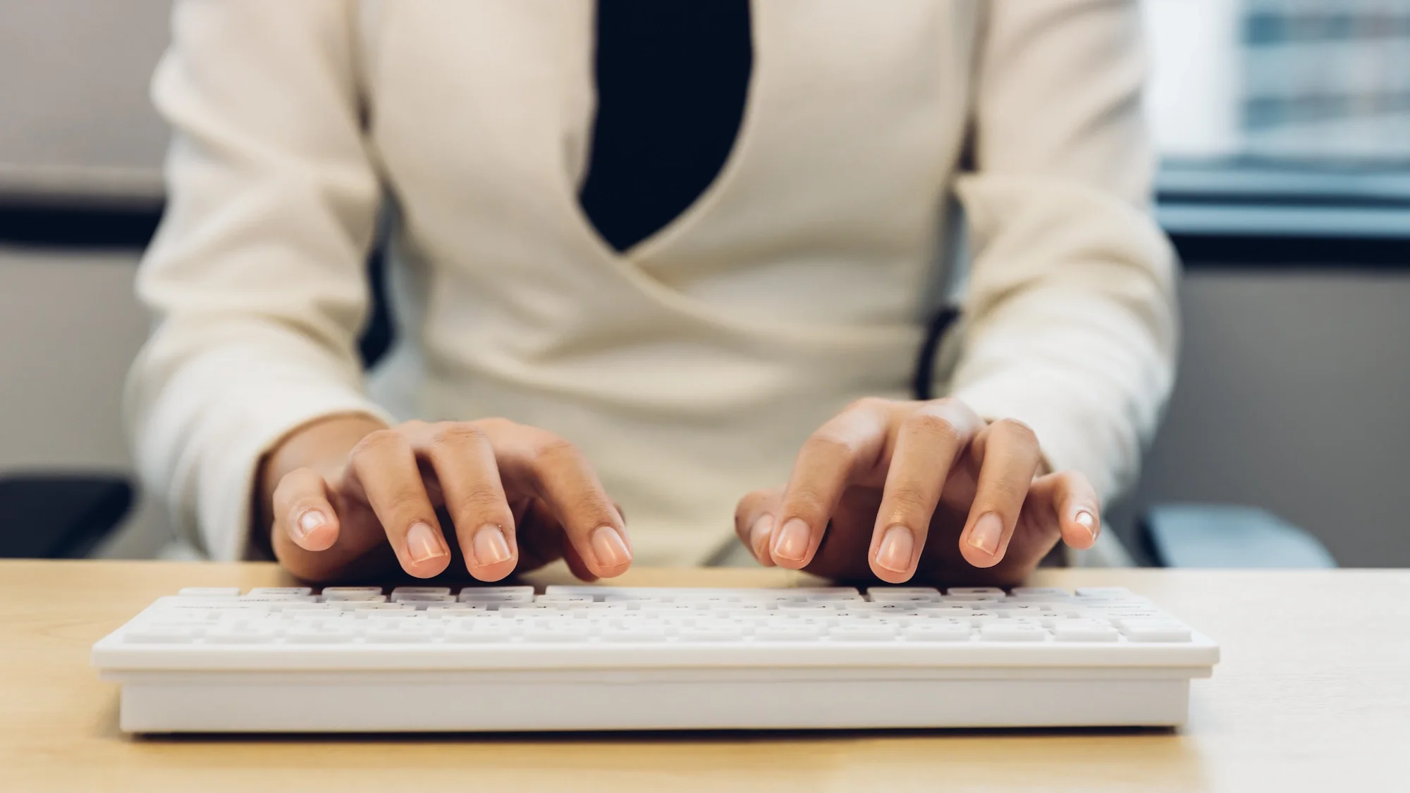 Person wearing a white shirt typing on a white keyboard at a desk in an office.