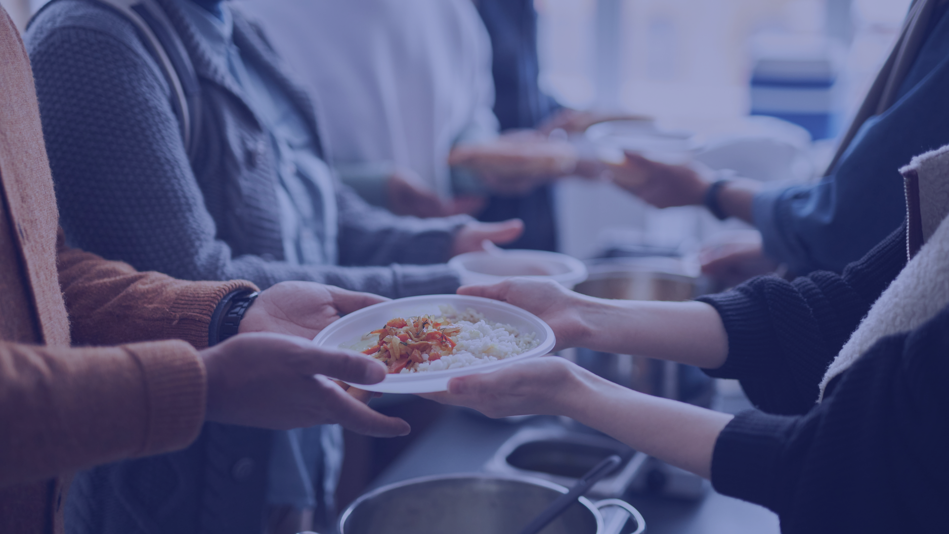 People in line at a food pantry or food bank, with a focus on hands exchanging a plate of food with rice and vegetables.