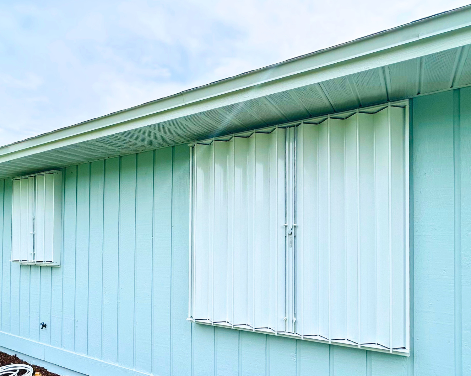 Side of a light mint green house with a closed window with metal security bars and a closed door, under a cloudy sky.