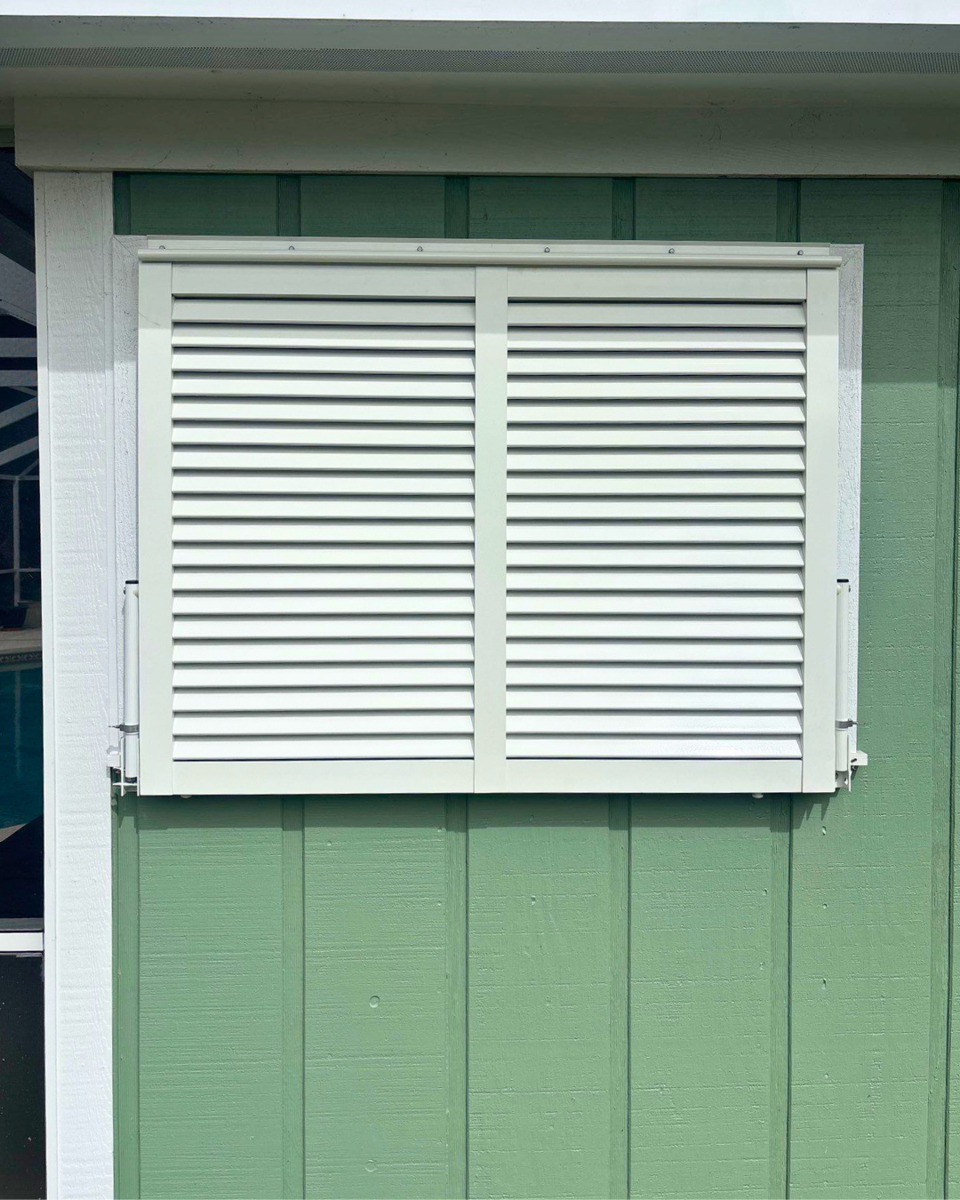 Green exterior wall with a white Bahama shutter window covering.