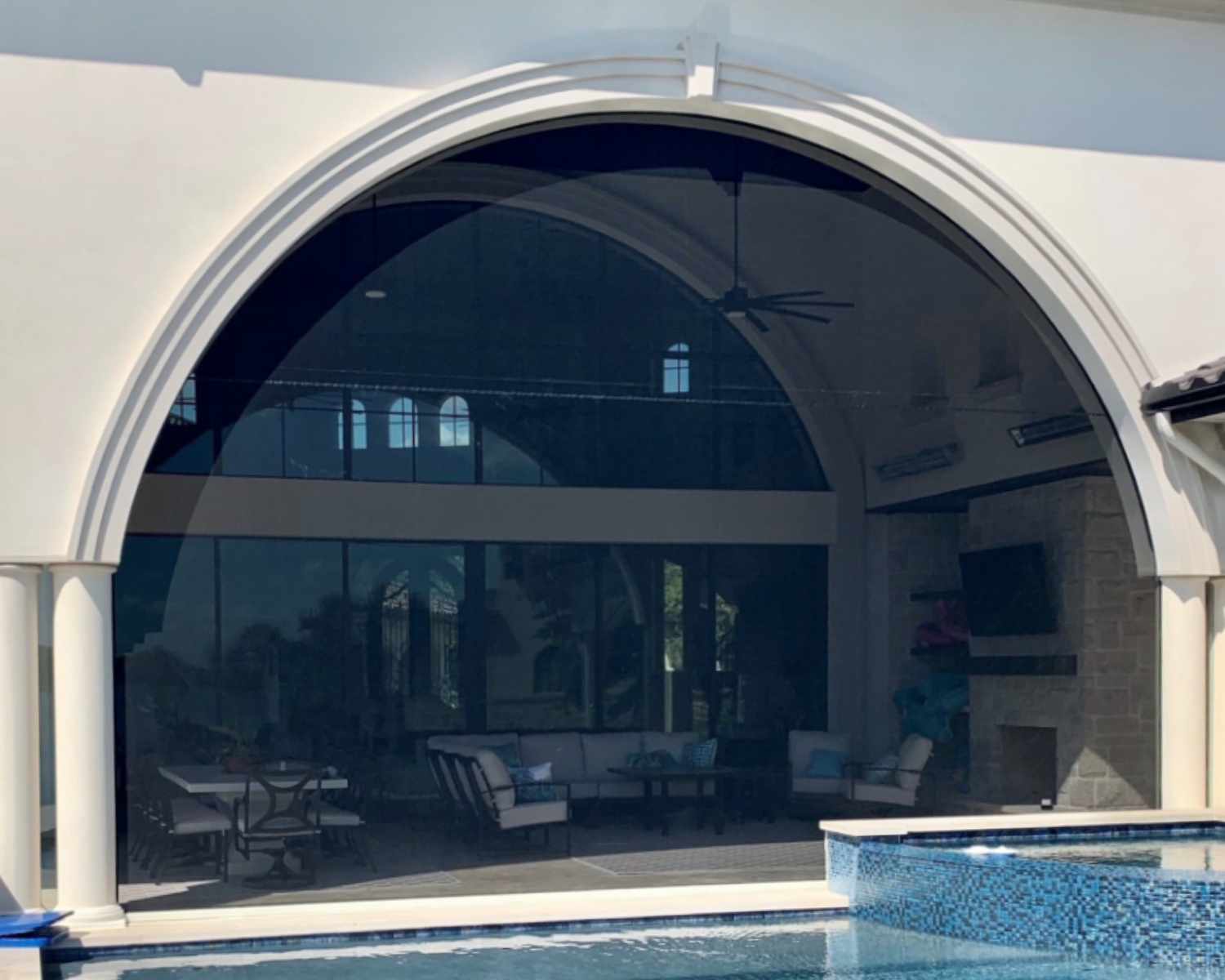 View of a house with a large arched window, a porch with a sitting area, and a swimming pool in the foreground.