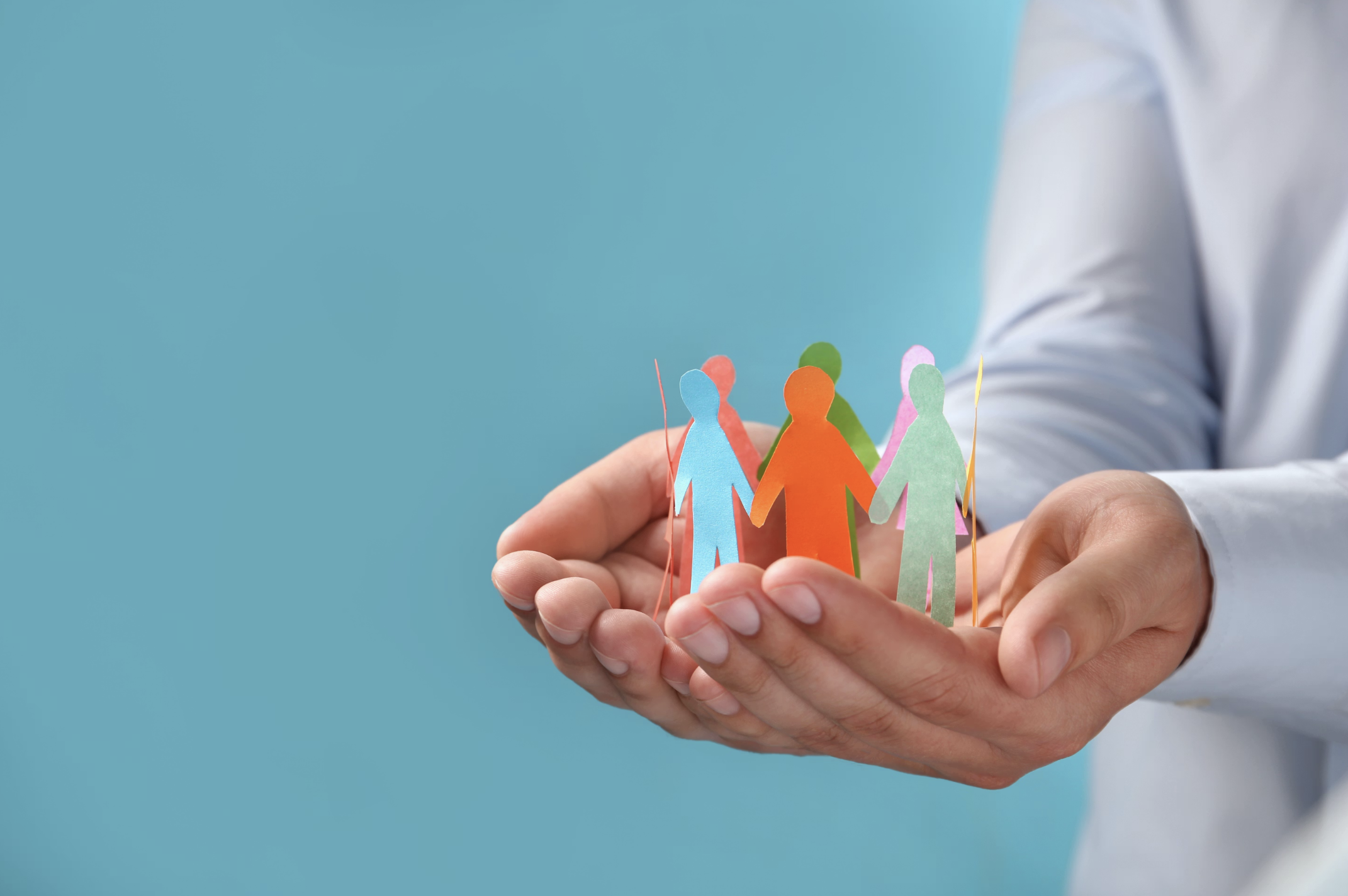 Person holding paper cutouts of multicolored human figures linked together in a circle.