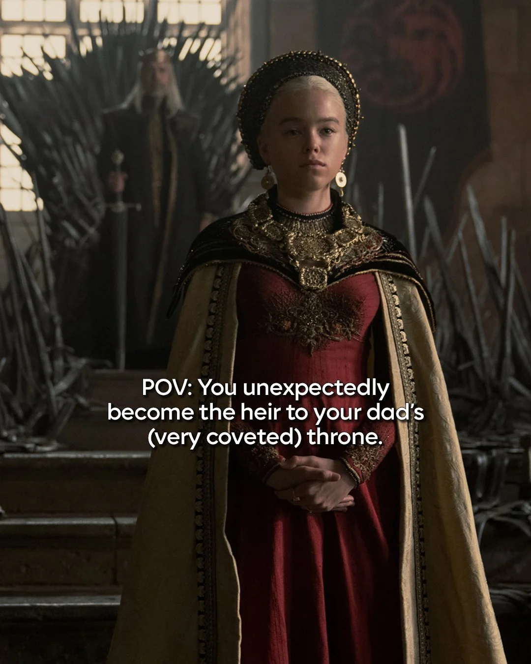 A woman dressed in regal medieval attire, wearing a red gown and ornate gold jewelry, stands in front of a throne with a stern expression, with another figure sitting on the throne in the background.