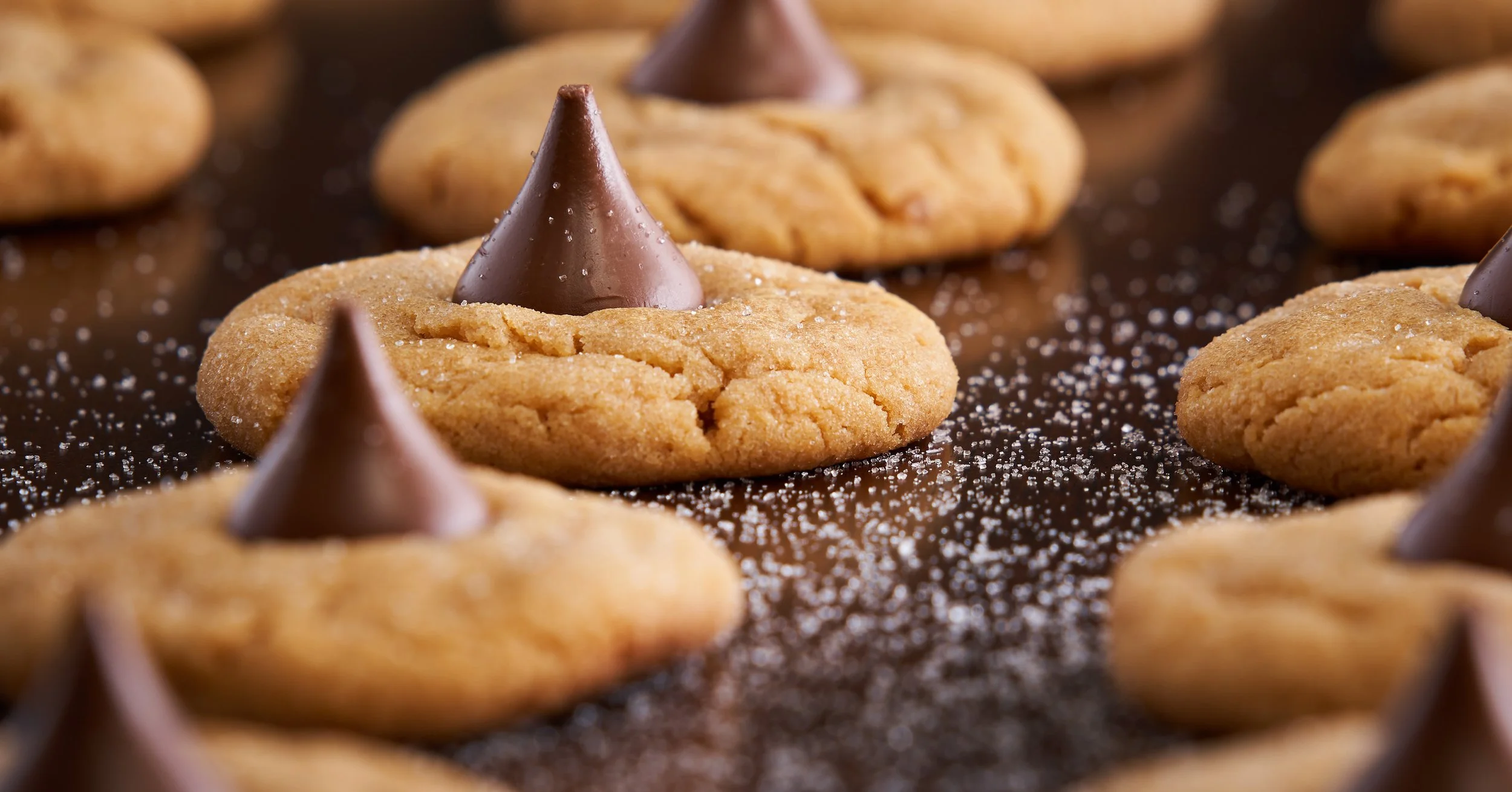 Close-up of chocolate chip cookies with a melted chocolate kiss in the center, sprinkled with powdered sugar.
