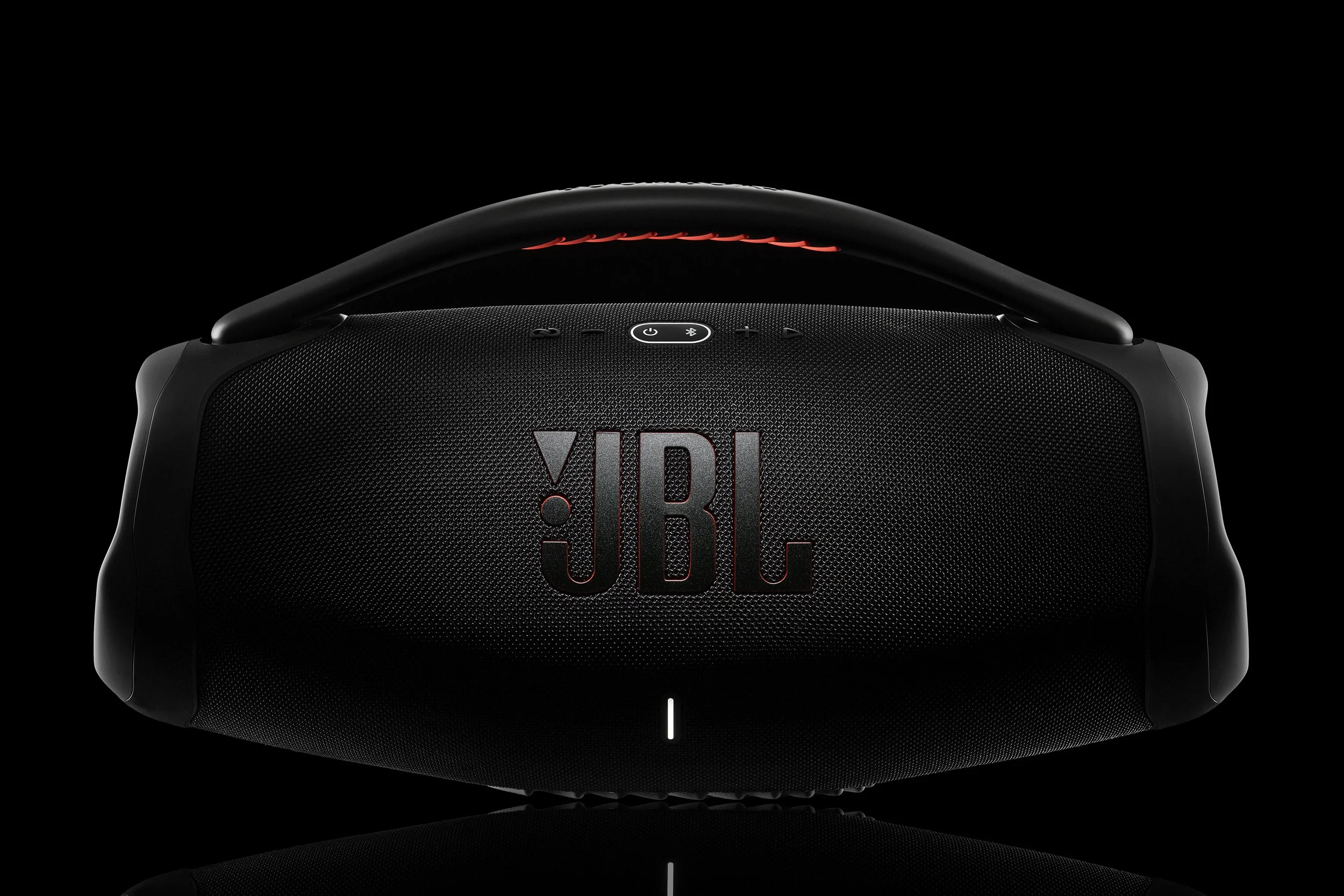 Black JBL portable Bluetooth speaker with carrying handle, illuminated control buttons, and red lighting accents, against a dark background.