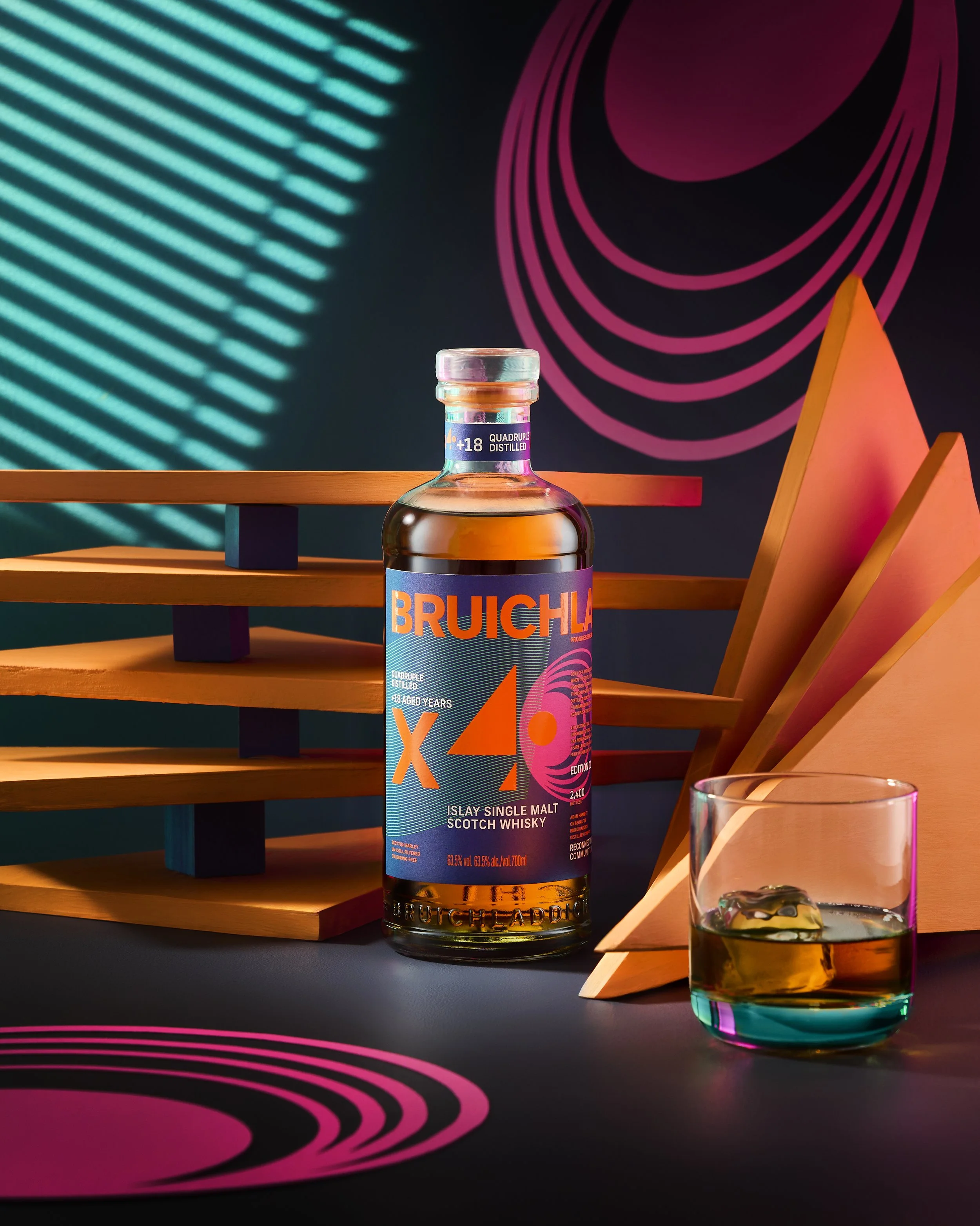 A bottle of Bruichladdich X4 whisky and a glass with ice on a dark surface, with colorful abstract background and geometric shapes.