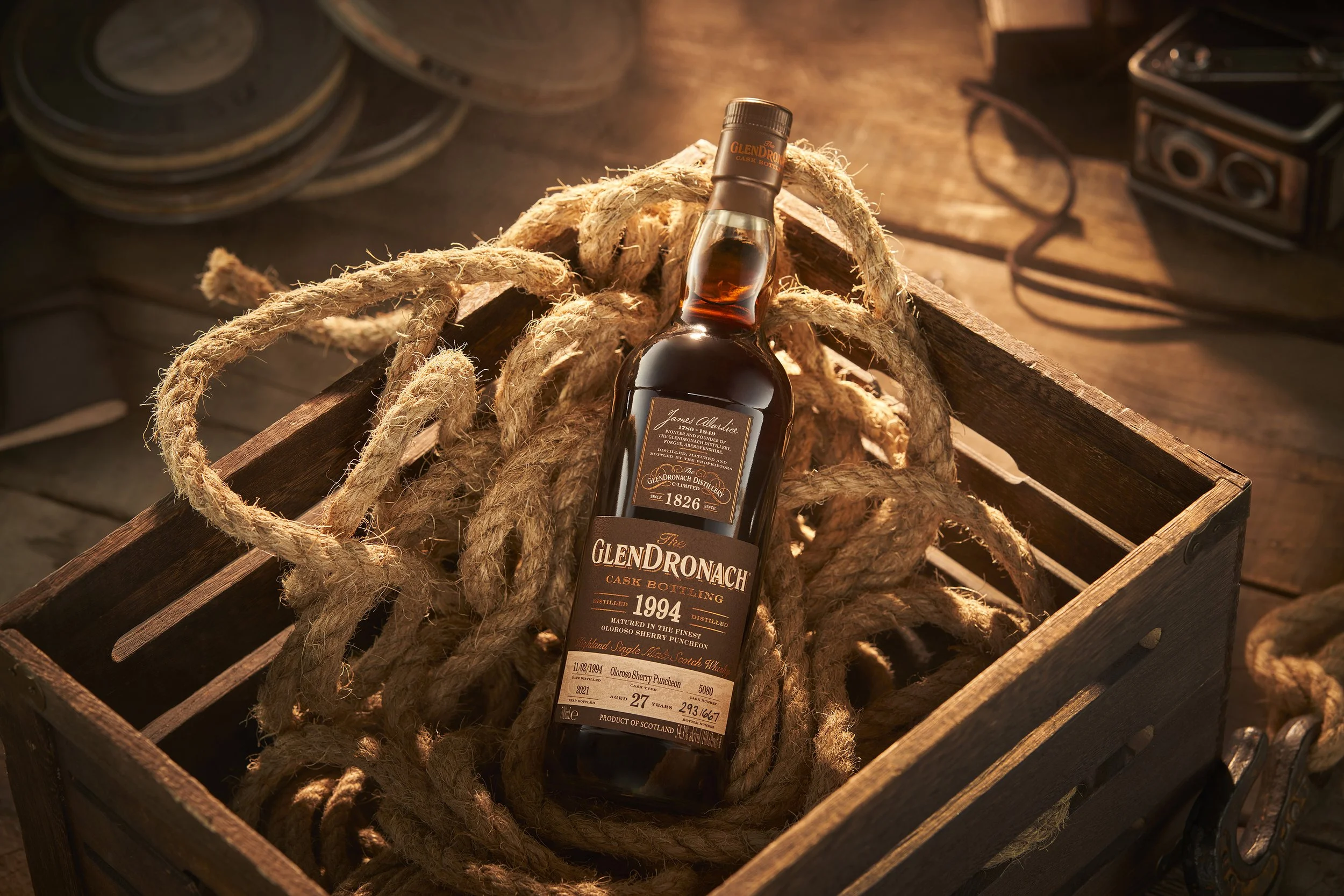 A bottle of Glendronach single malt Scotch whisky lying in a wooden crate surrounded by thick, rustic ropes.